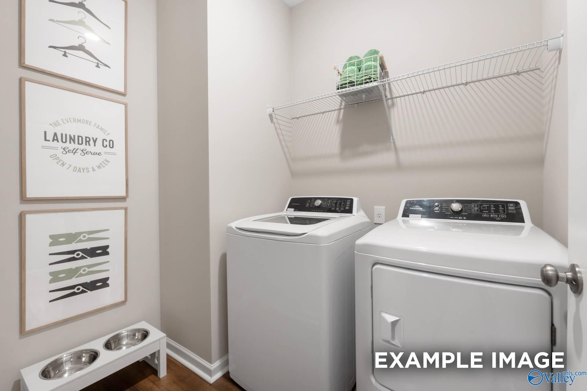 Modern laundry room with white washer-dryer set, hanging shelves, green towels, and skateboard art in Davidson Homes The Stella, Madison AL