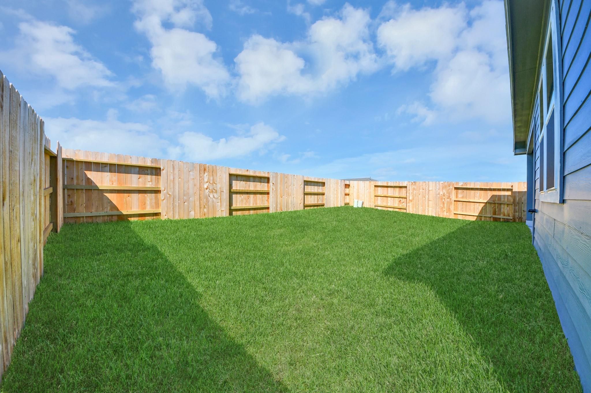 Private fenced backyard with lush green grass at The Riviera A home in Emberly, Beasley, Texas.