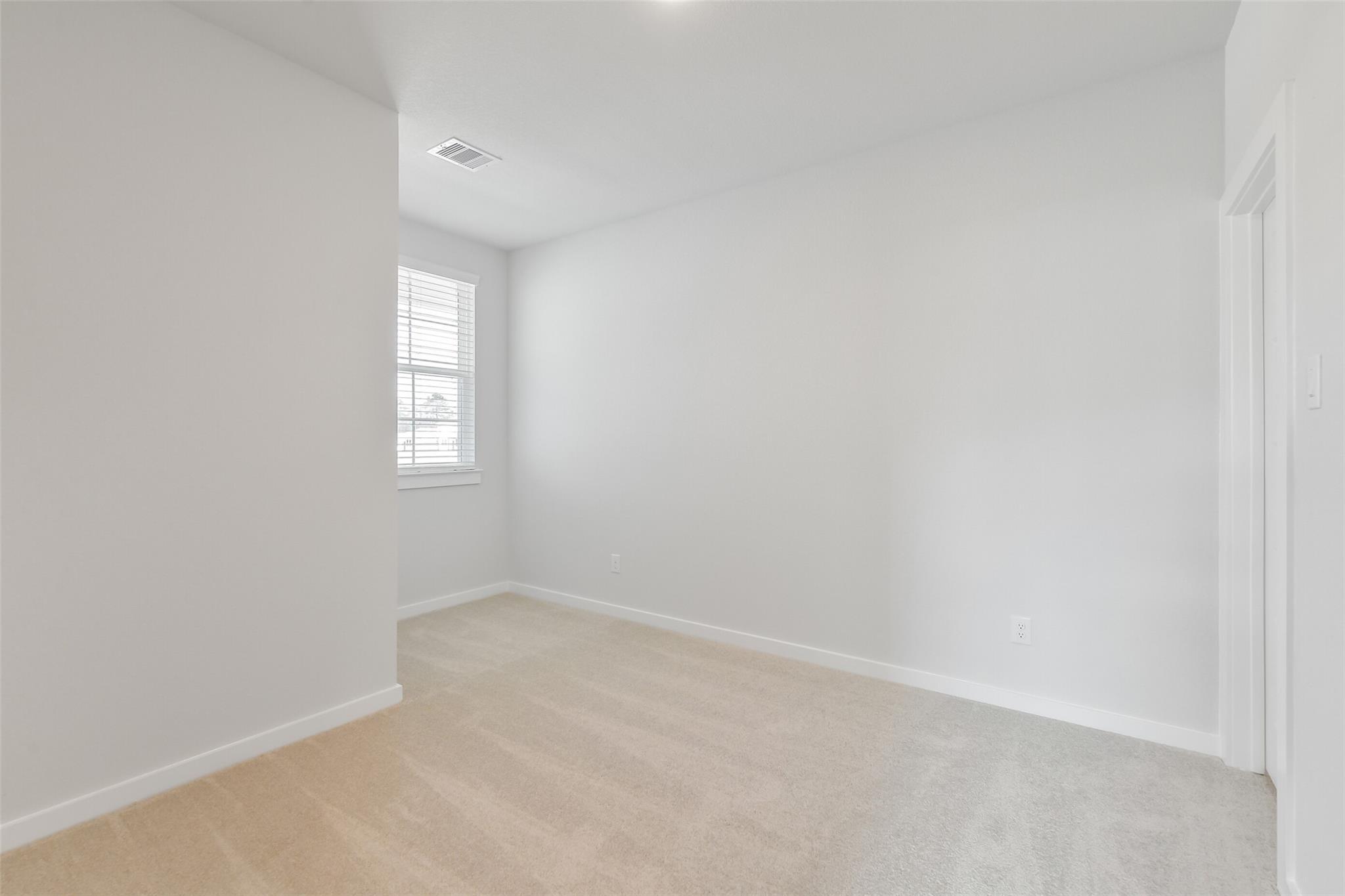 Empty bedroom with white walls, large window, hardwood floors, and carpet in Davidson Homes The Colorado F, Cleveland, Texas