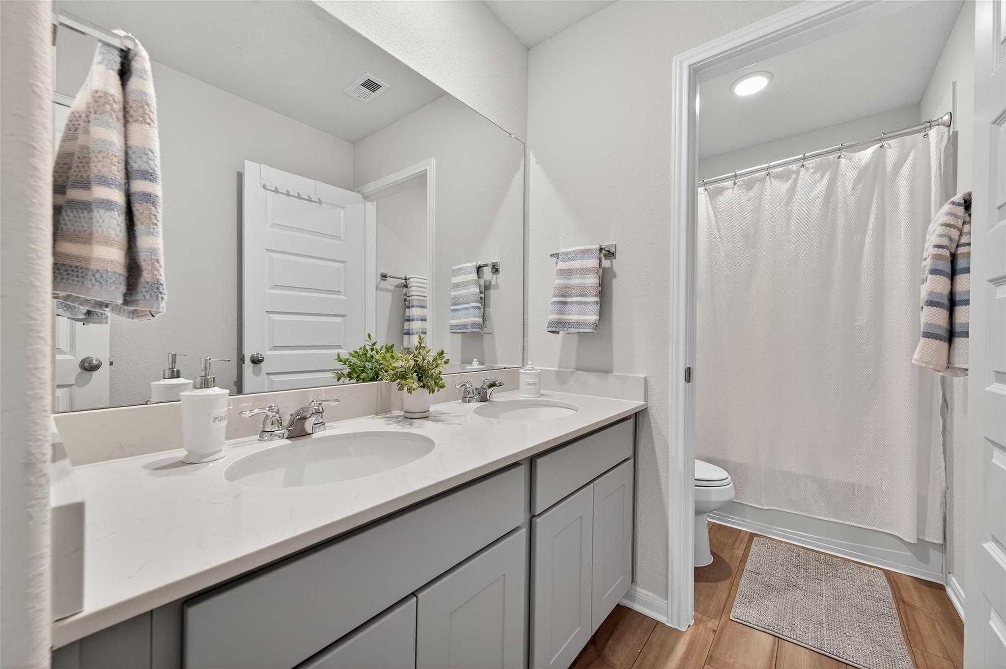 Modern secondary bathroom with double vanity, gray cabinets, white quartz counters, and walk-in shower in Davidson Homes The Brazos E, Magnolia, Texas