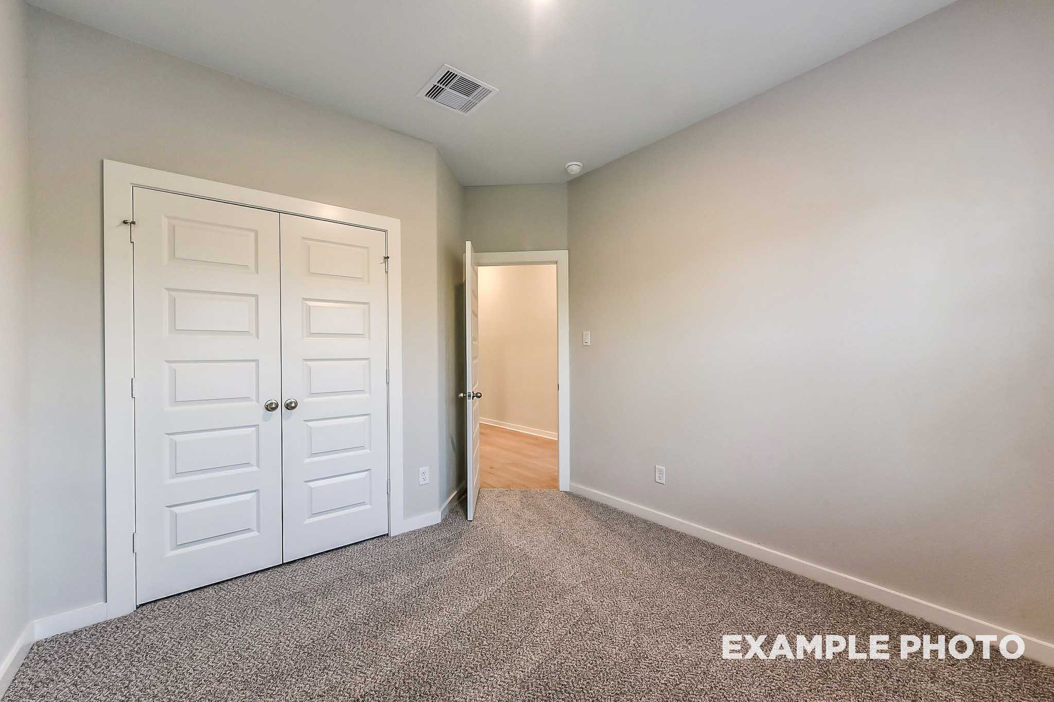 Spacious master bedroom in The Laguna B with double closet doors, open bathroom entry, gray walls and carpet flooring