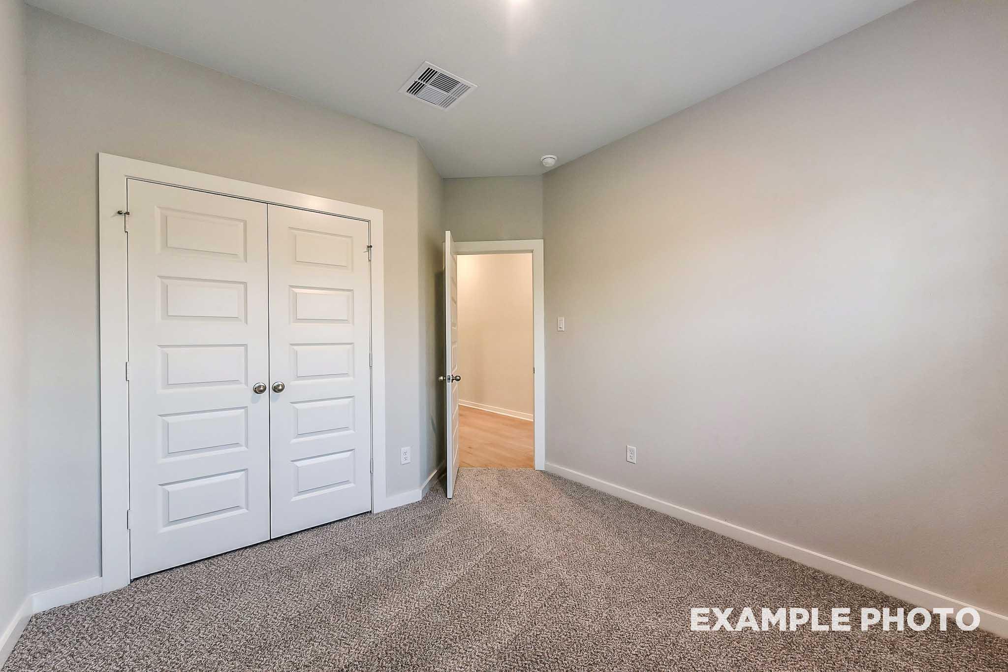 Spacious master bedroom in The Laguna B with double closet doors, open bathroom entry, gray walls and carpet flooring