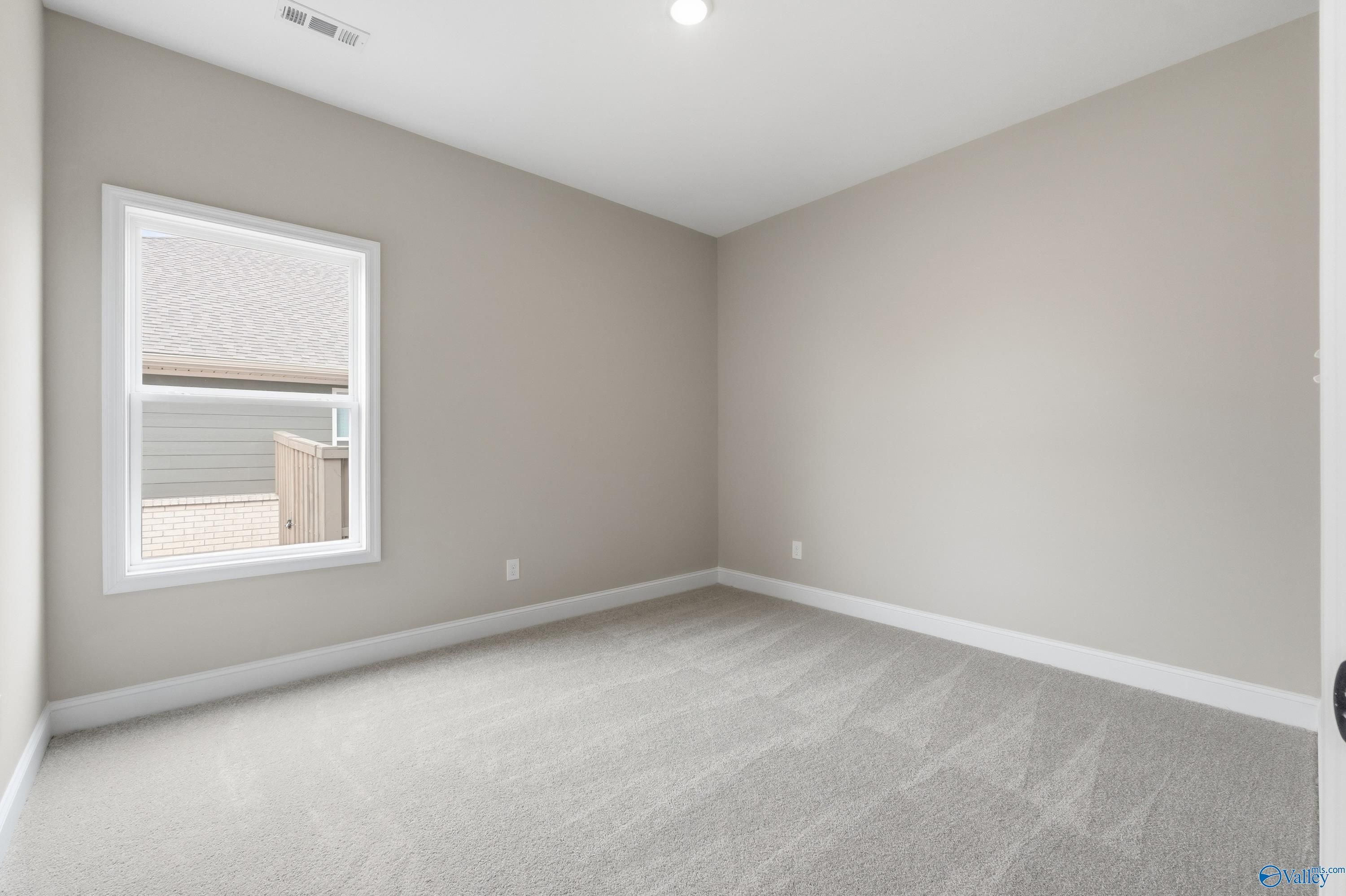 Cozy secondary bedroom with neutral beige walls, plush carpet, and large window in The Rockford C by Davidson Homes, Athens, AL