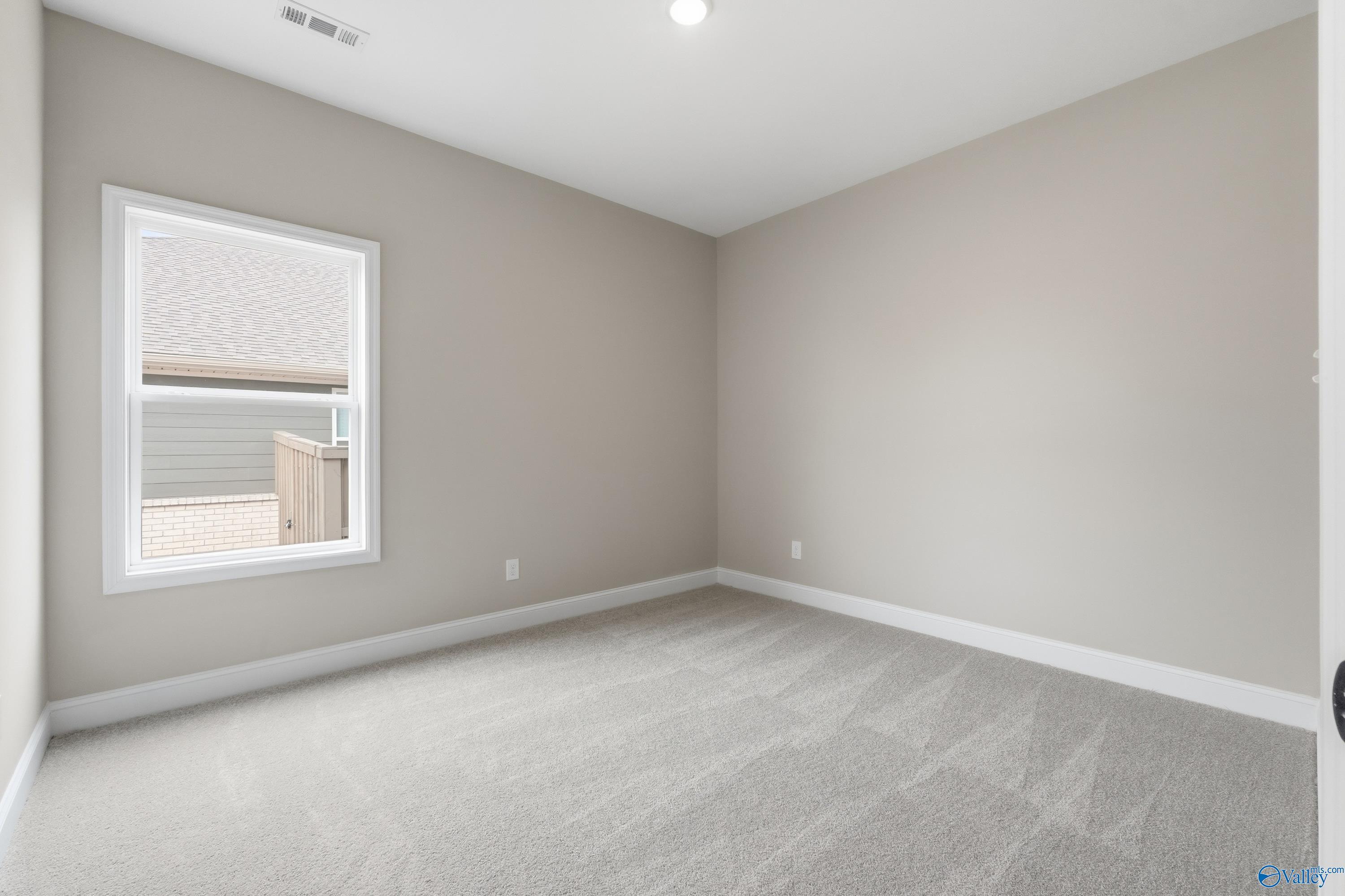 Cozy secondary bedroom with neutral beige walls, plush carpet, and large window in The Rockford C by Davidson Homes, Athens, AL