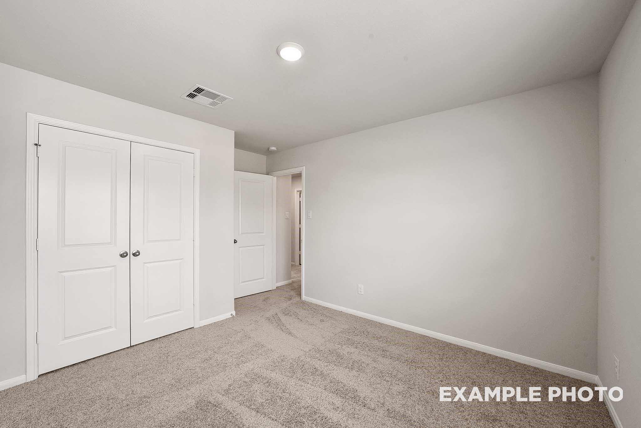 Empty secondary bedroom with double closet doors, beige walls, and carpet flooring in Davidson Homes The Tierra B, Beasley, Texas