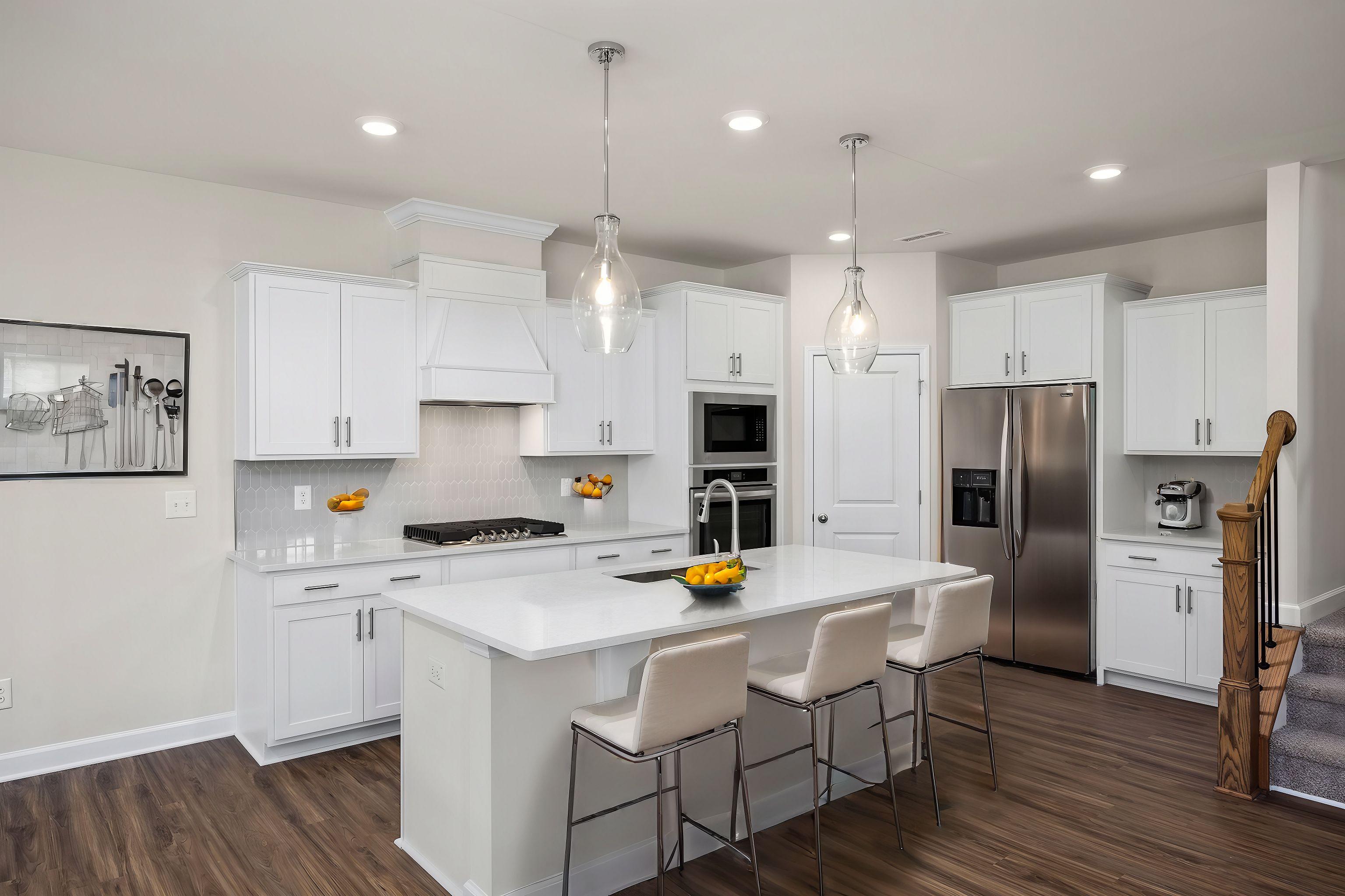 Spacious white kitchen in The Grace A by Davidson Homes featuring large island, bar stools, stainless appliances, and hardwood floors