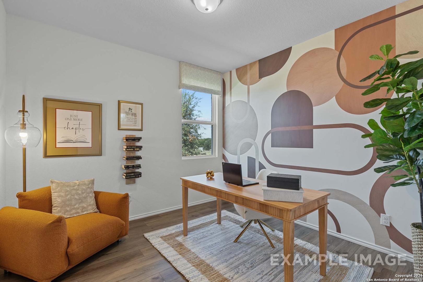 Modern home office with wooden desk, dual monitors, orange armchair, potted plant, and geometric wall art in The Daphne K, San Antonio