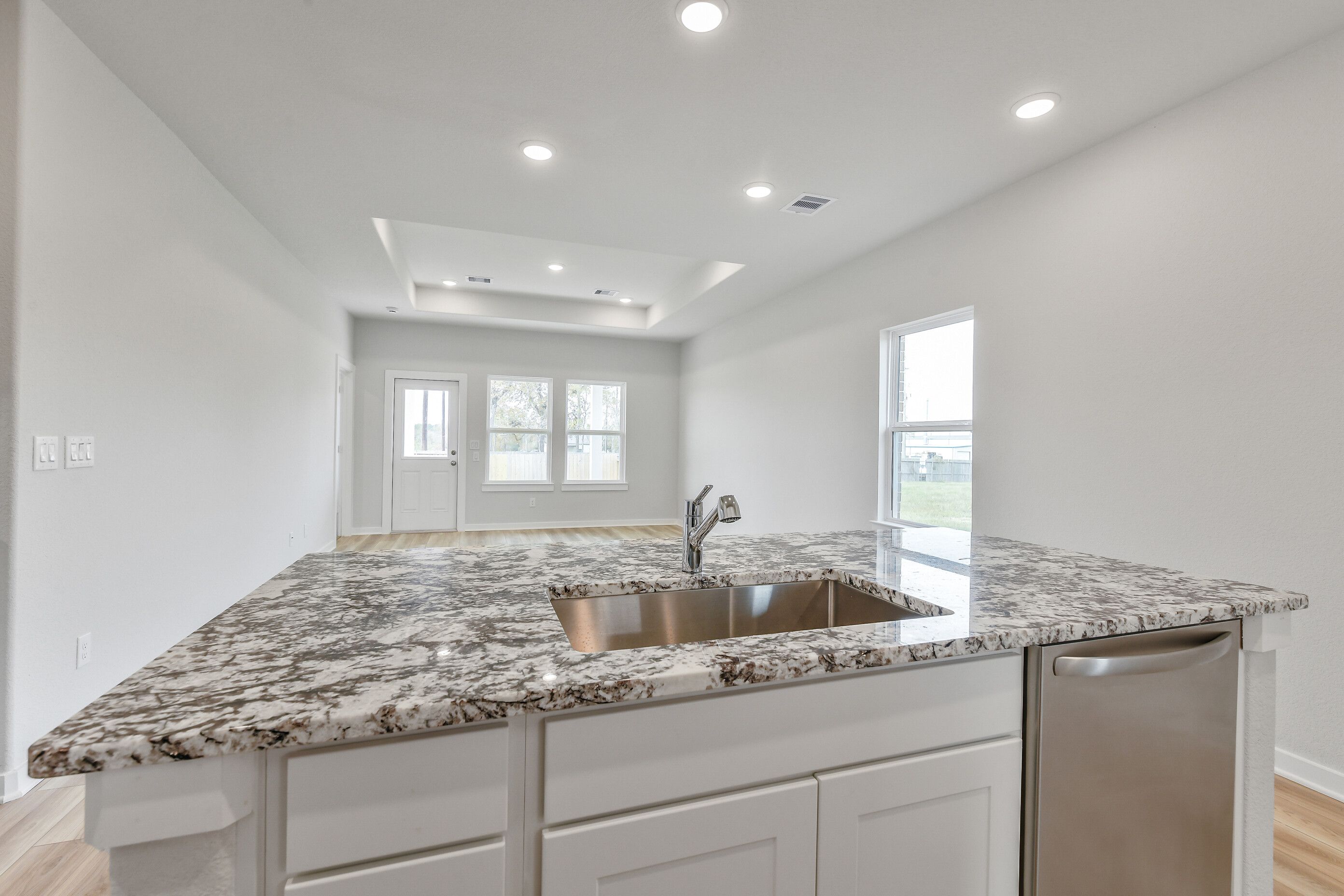 Modern kitchen island with granite countertop, stainless sink, dishwasher, and white cabinets in Davidson Homes The Colorado G, Magnolia, Texas