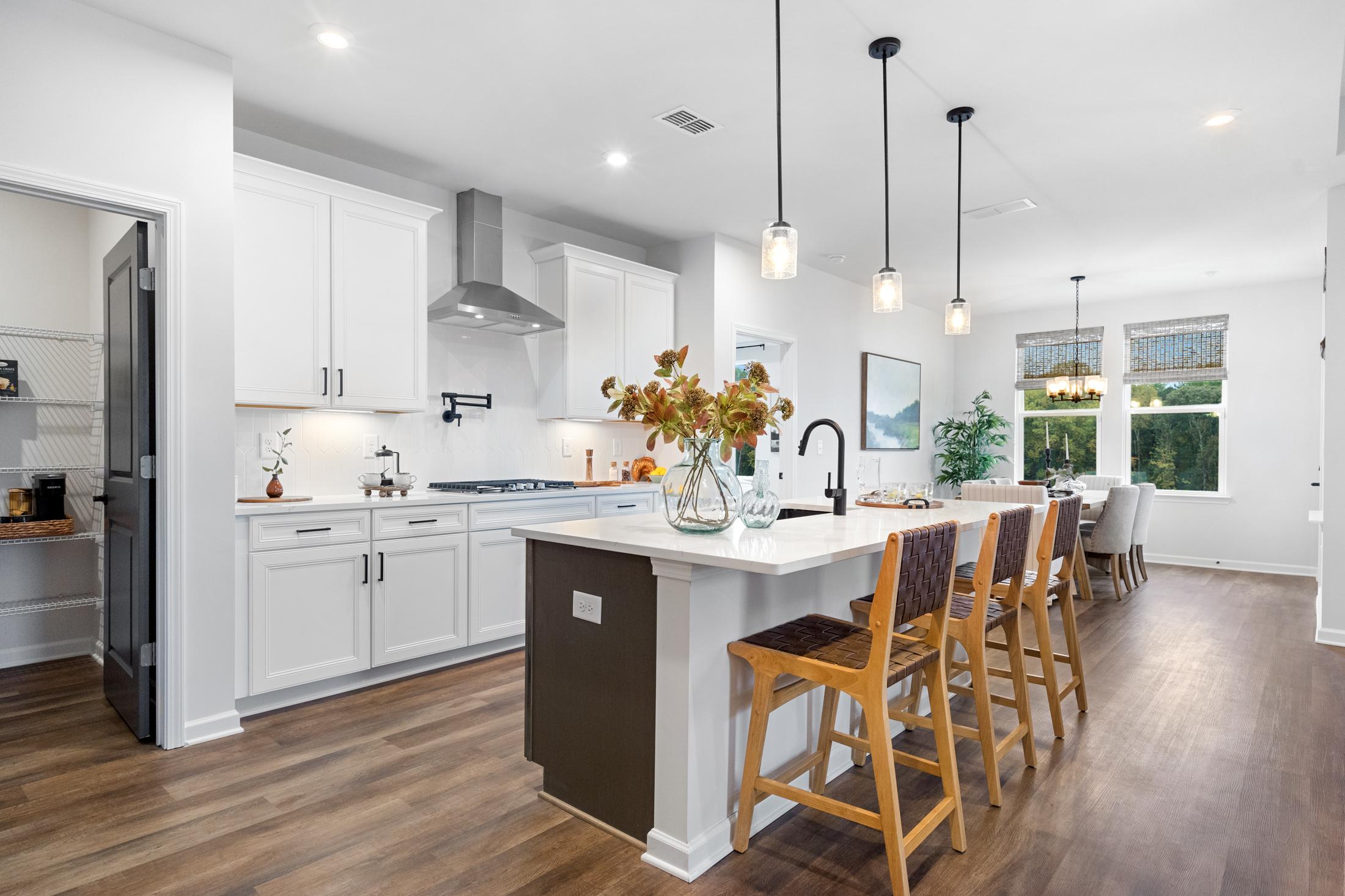 Spacious modern kitchen in The Edison A with white island, bar stools, stainless steel hood, and pendant lights