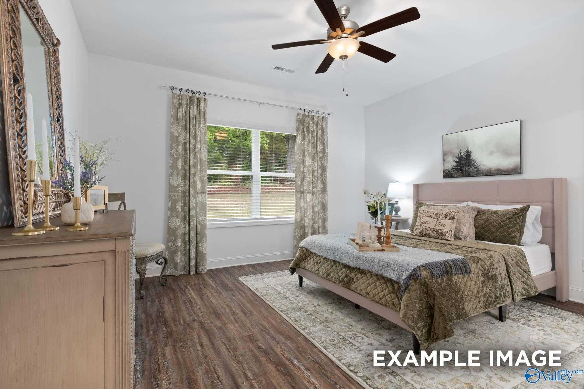 Cozy bedroom with queen bed, neutral bedding, hardwood floors, ceiling fan, and large window in Davidson Homes The Cumberland B, Decatur, Alabama