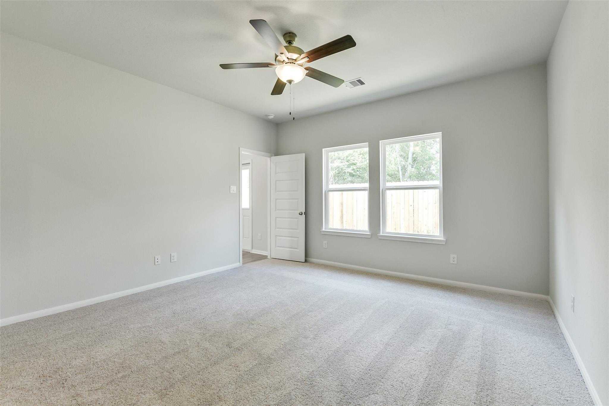 Bright empty bedroom with ceiling fan, double windows, gray walls, and carpet in Davidson Homes The Sabine E, Conroe, Texas