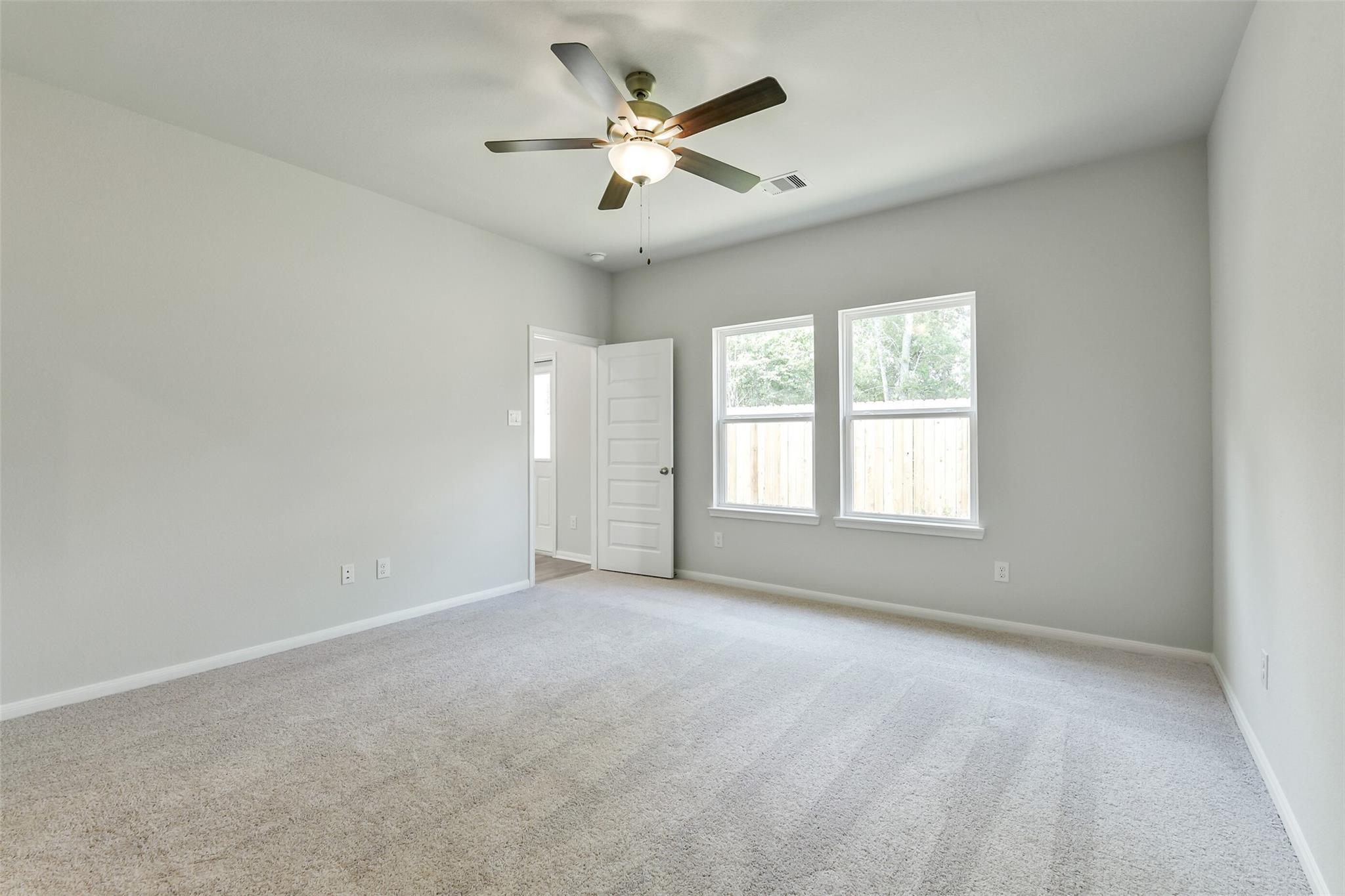 Bright empty bedroom with ceiling fan, double windows, gray walls, and carpet in Davidson Homes The Sabine E, Conroe, Texas