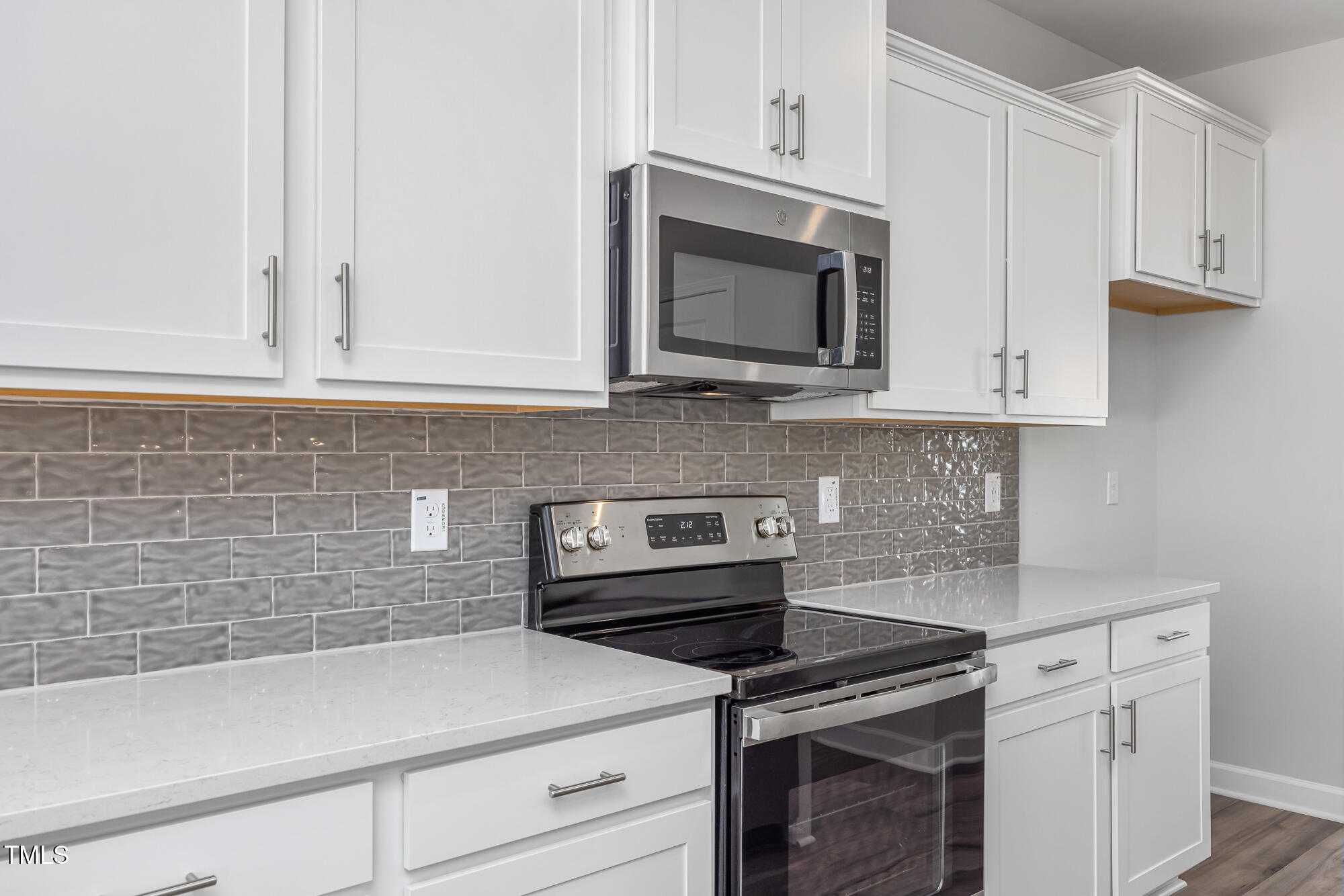 Modern kitchen with white cabinets, stainless steel appliances, quartz counters, and gray subway tile in Davidson Homes The Willow C, Angier, NC