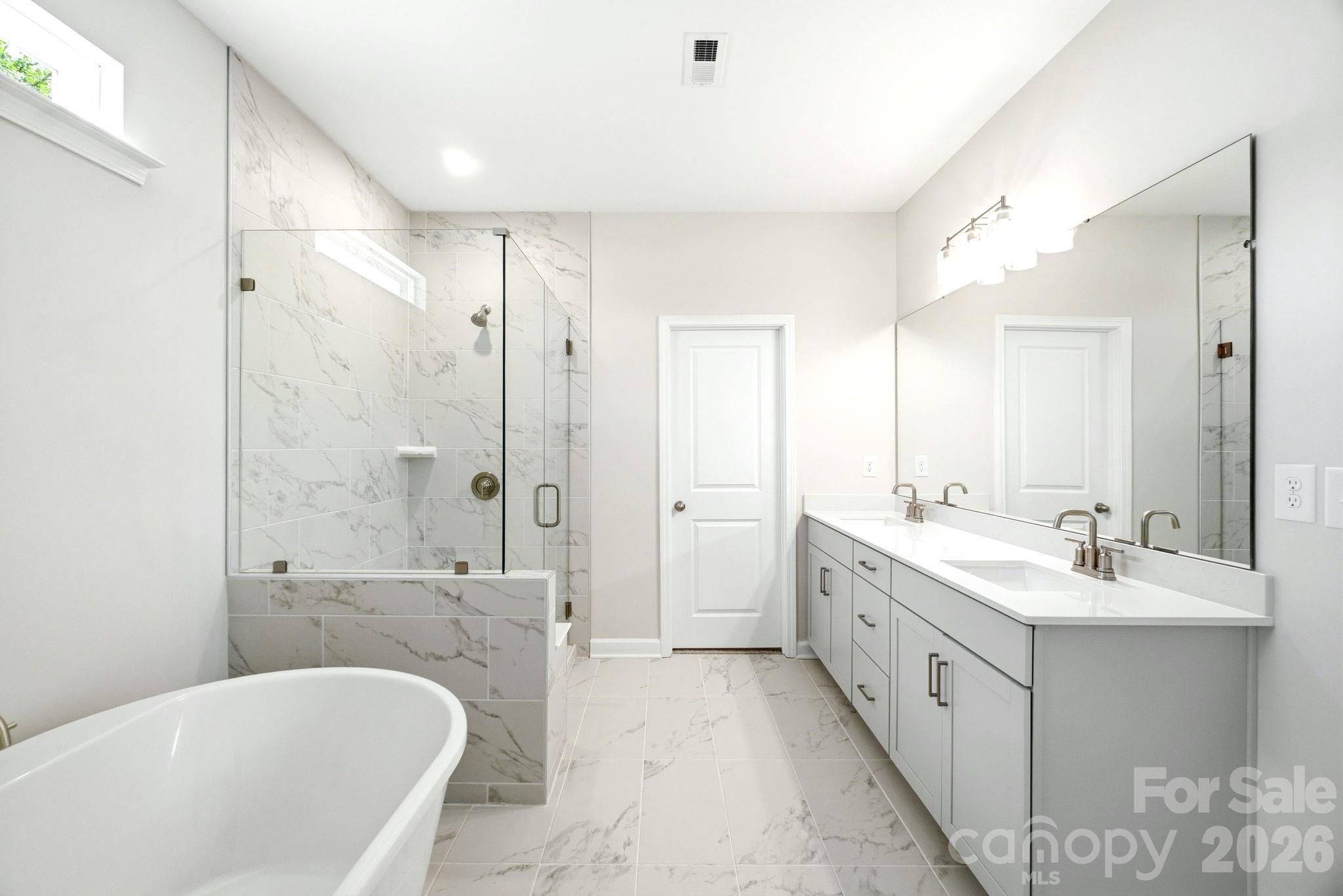 Modern primary bathroom with marble tile, glass-enclosed shower, soaking tub, and dual vanity in Windgate, Mooresville.