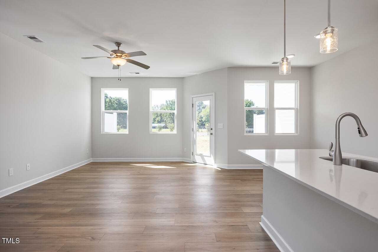 Bright open-concept living-kitchen with hardwood floors, white island, pendant lights, and large windows in The Graham home, Fuquay-Varina, NC