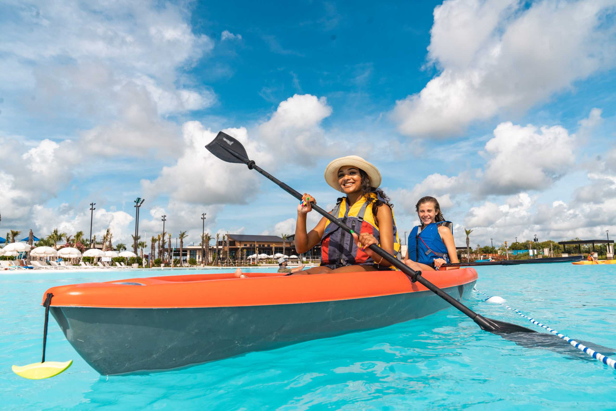 Women kayaking on turquoise lagoon at Lago Mar in Texas City Texas with palm trees and resort umbrellas