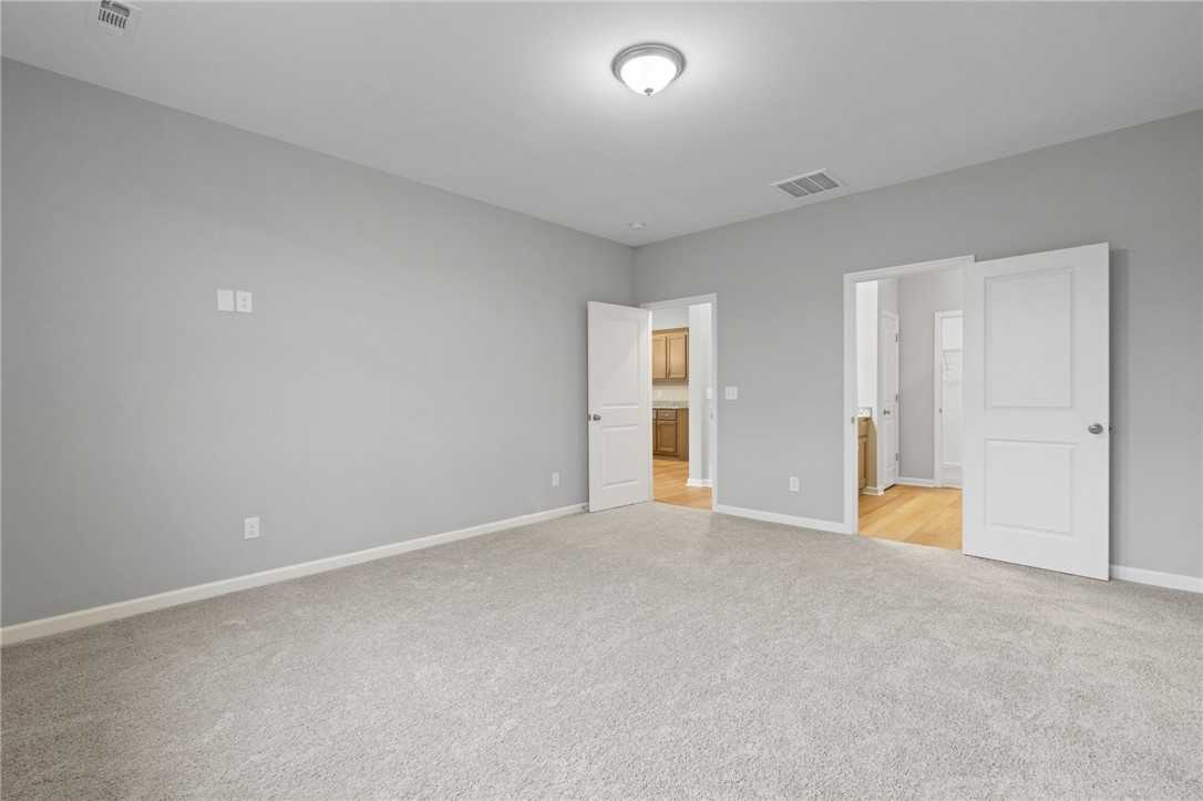 Spacious master bedroom with gray walls, carpet floor, and en-suite bath doors in Davidson Homes The Luna B, Opelika AL