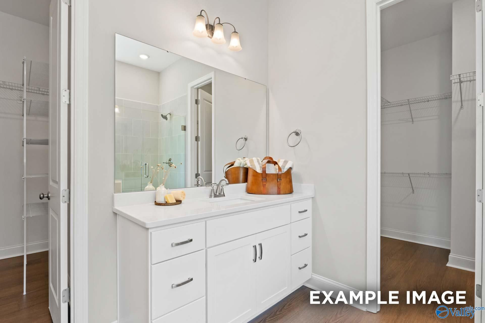 Elegant master bathroom with white quartz vanity, large mirror, and adjacent walk-in closet in Evermore Homes The Haven E, Owens Cross Roads, Alabama