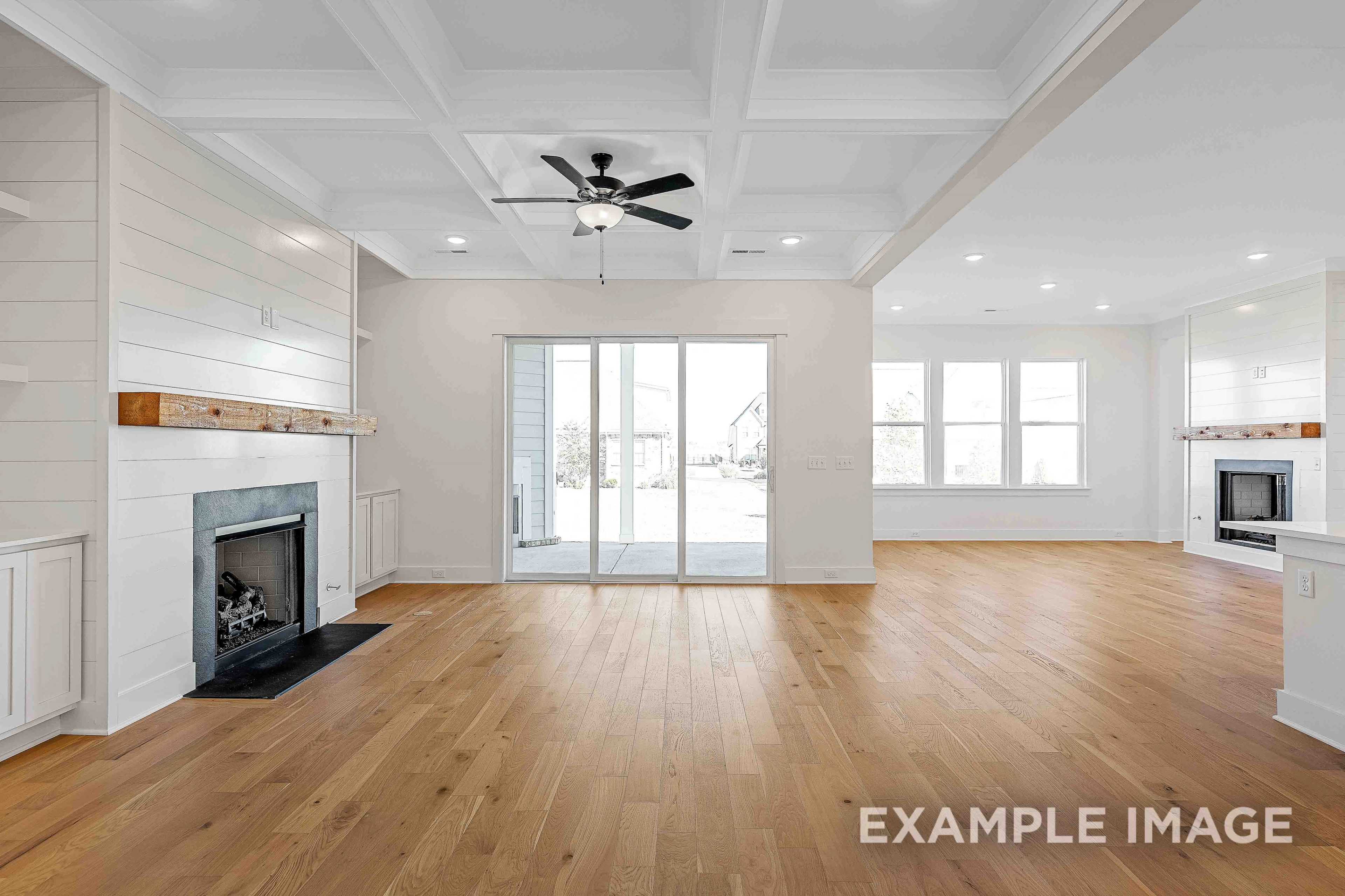 Spacious open-concept great room in The Albany A featuring dual fireplaces, hardwood floors, and sliding doors to patio