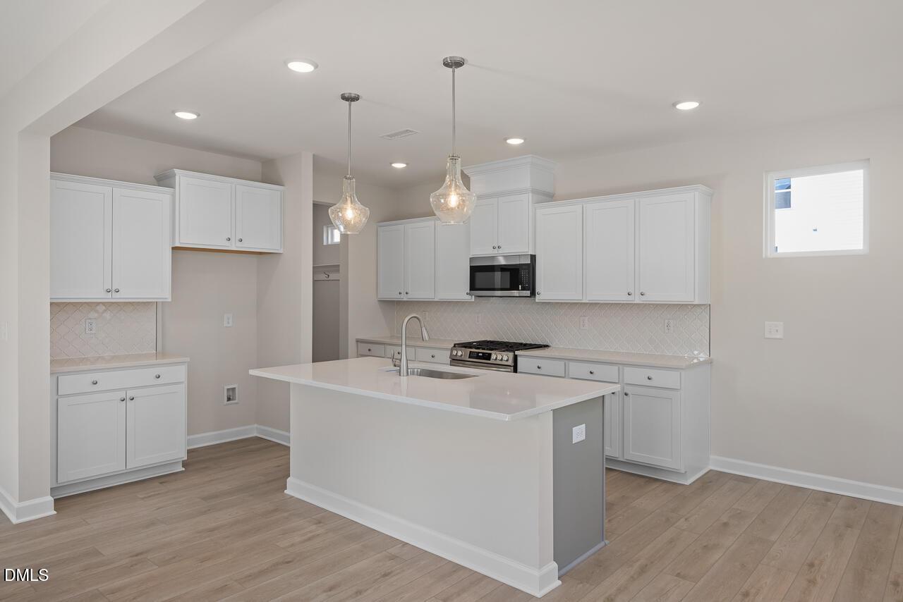 Modern white shaker kitchen with large island sink, stainless appliances, and pendant lights in The Gavin C by Davidson Homes, Lillington, NC