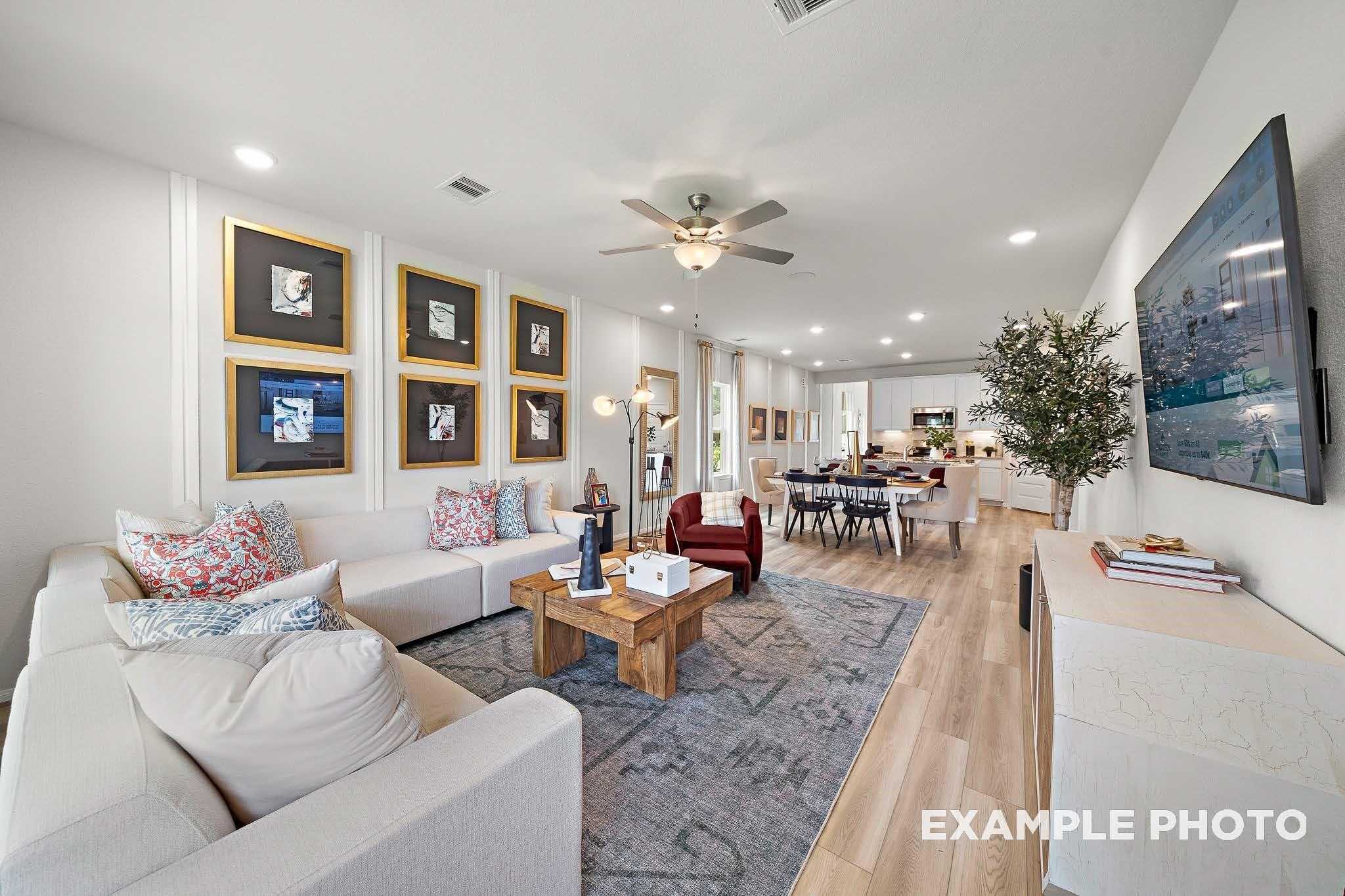 Bright open-concept living room with white sofas, wooden coffee table, ceiling fan, and wall TV in Davidson Homes San Marcos E, Conroe, Texas