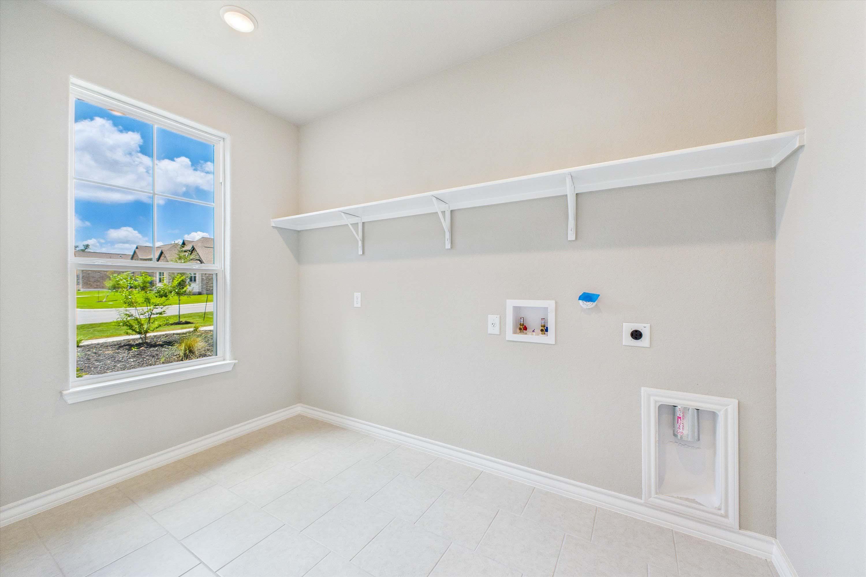 Bright laundry room in The Foster floor plan featuring tile flooring, wall shelving, and connections for appliances.