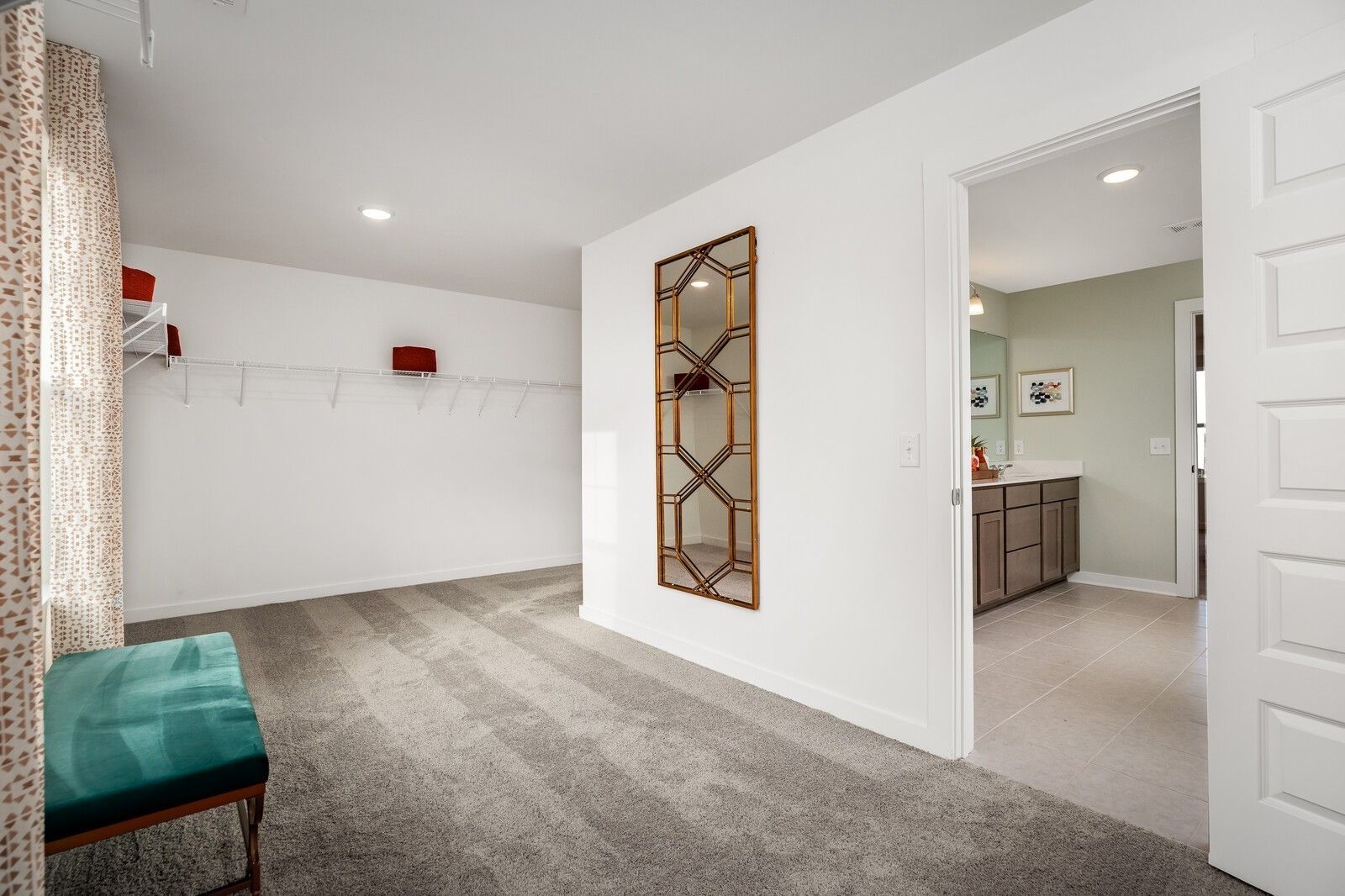 Elegant walk-in closet with gold geometric mirror, built-in shelving, and green bench opening to sage green master bathroom in Davidson Homes The Gordon C, White House TN