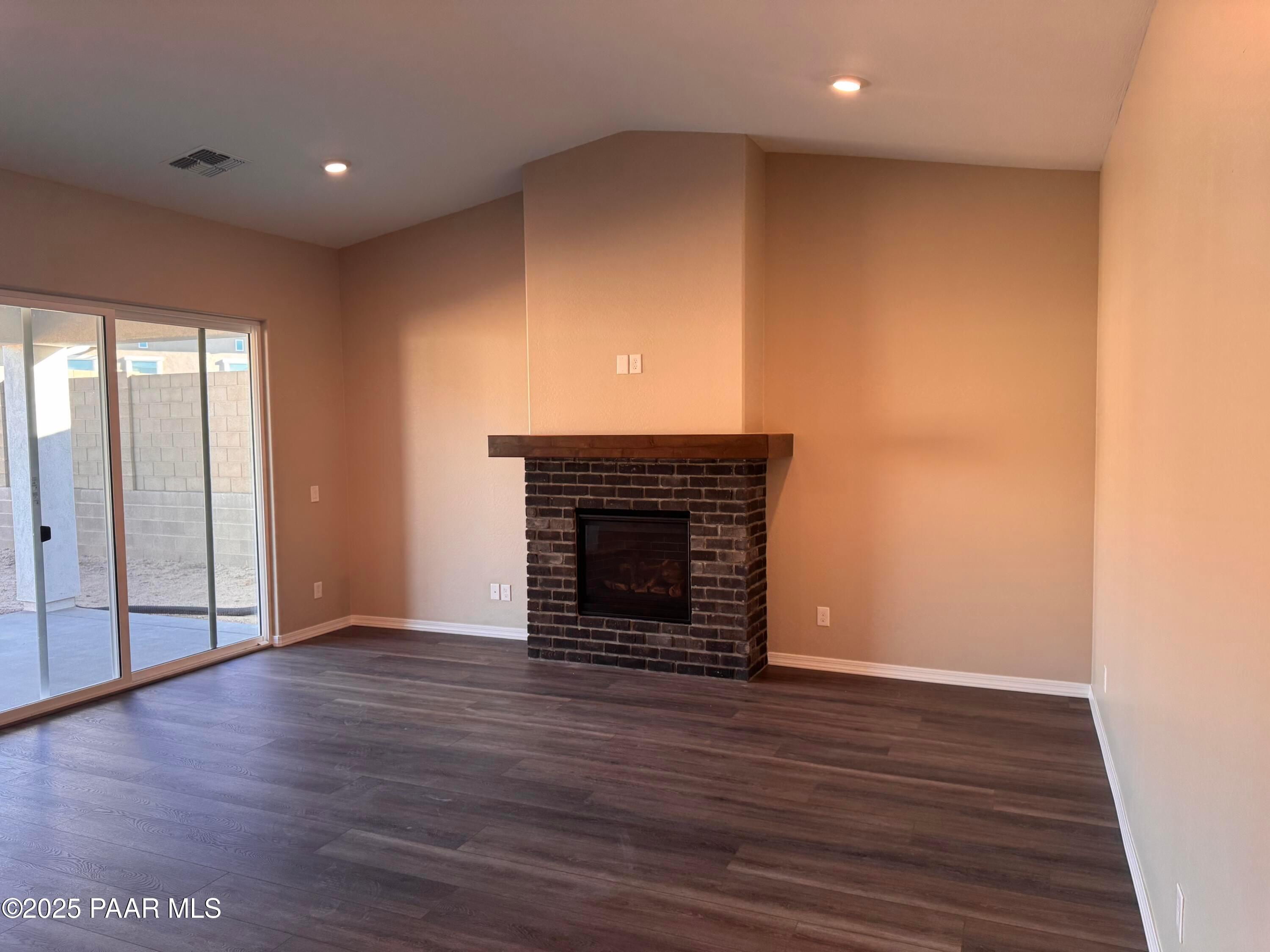 Cozy brick fireplace with wooden mantel in spacious living room, sliding doors to patio, Westwood Prescott Arizona home