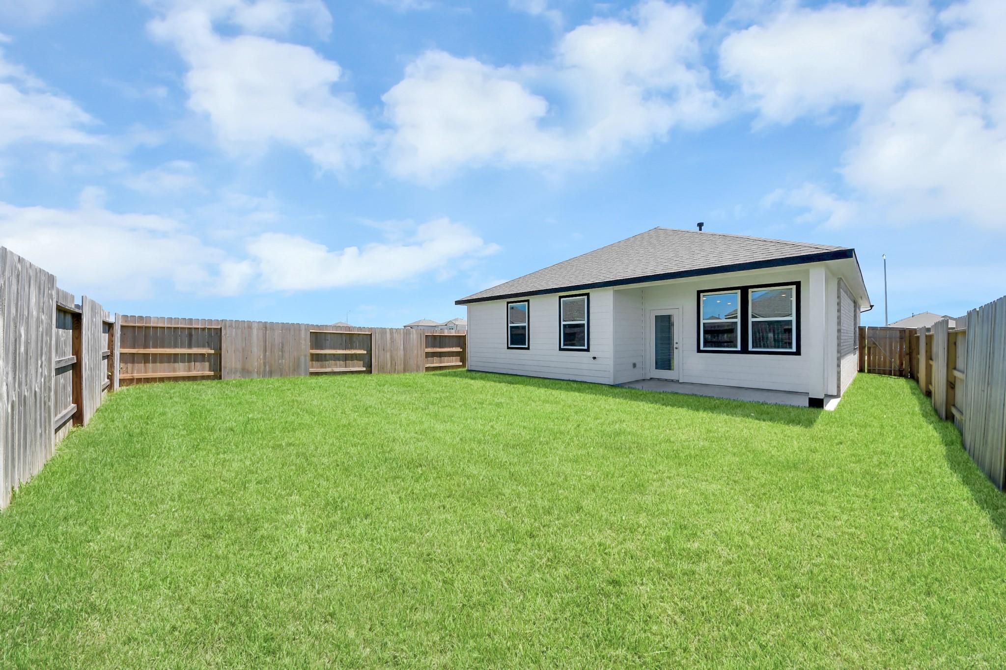 Spacious fenced backyard with lush green lawn at Davidson Homes The Costa A in Emberly, Beasley, Texas
