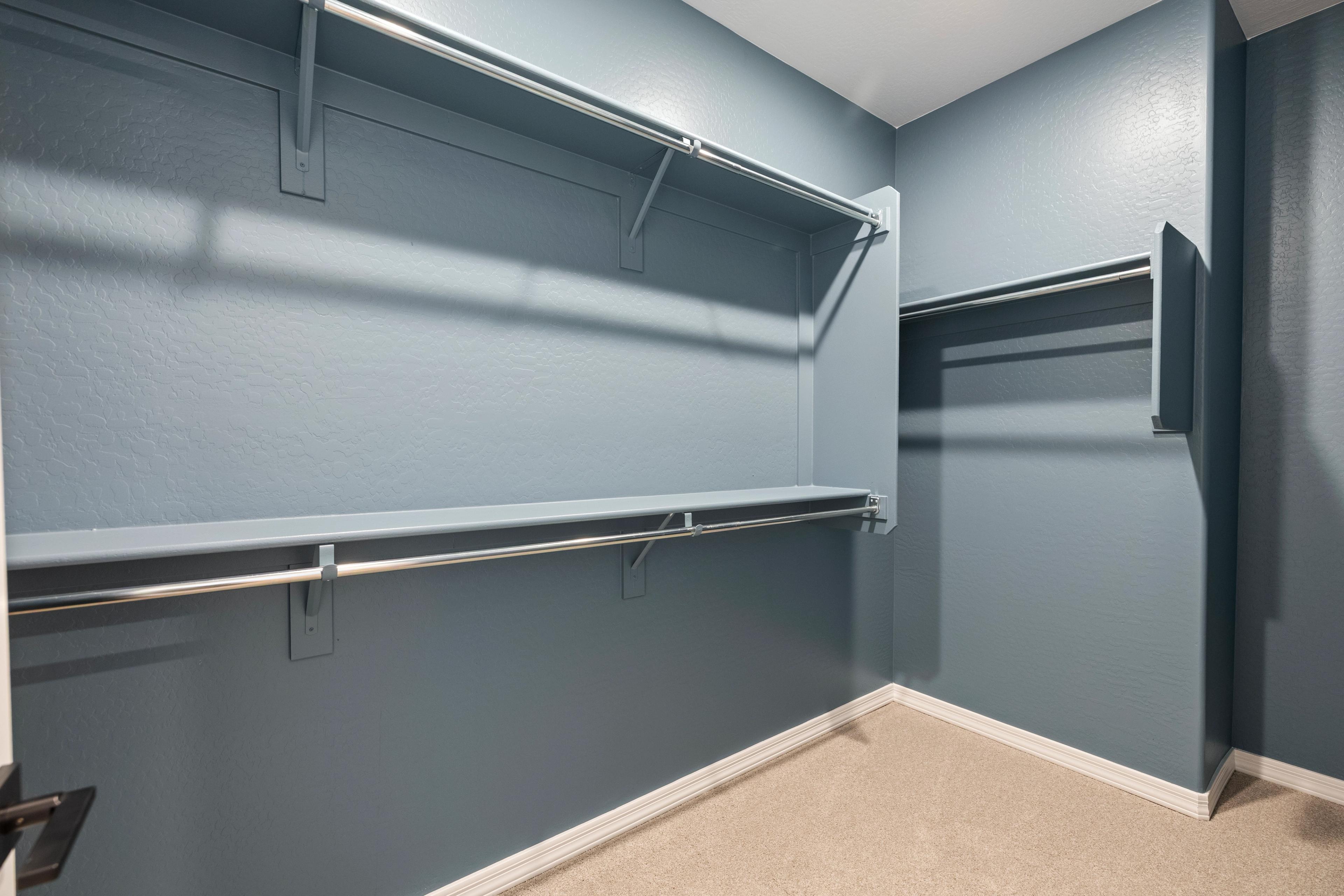 Spacious walk-in closet at Vineyards at Cottonwood in Cottonwood AZ with blue walls, double hanging rods, and built-in shelves