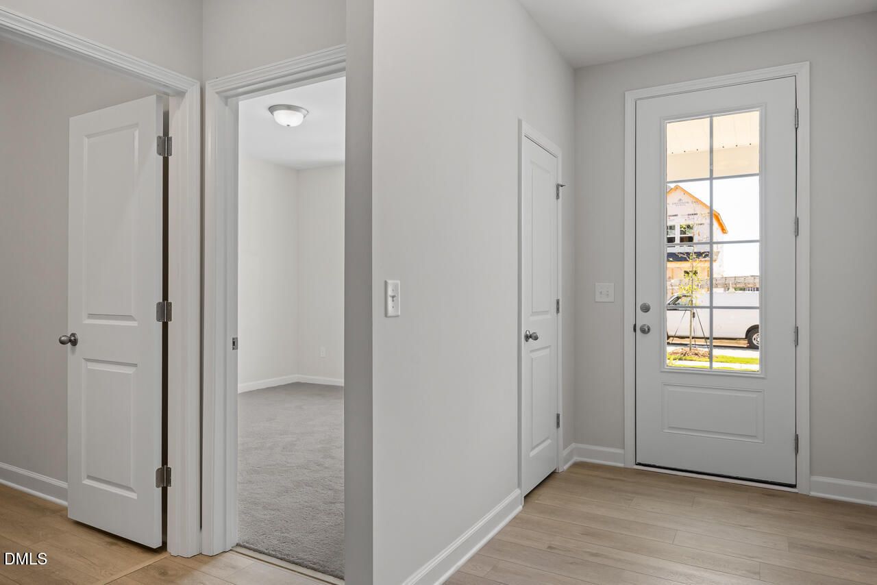 Bright foyer with glass-panel front door, hardwood floors, and carpeted bedroom in Davidson Homes Daphne D, Zebulon NC