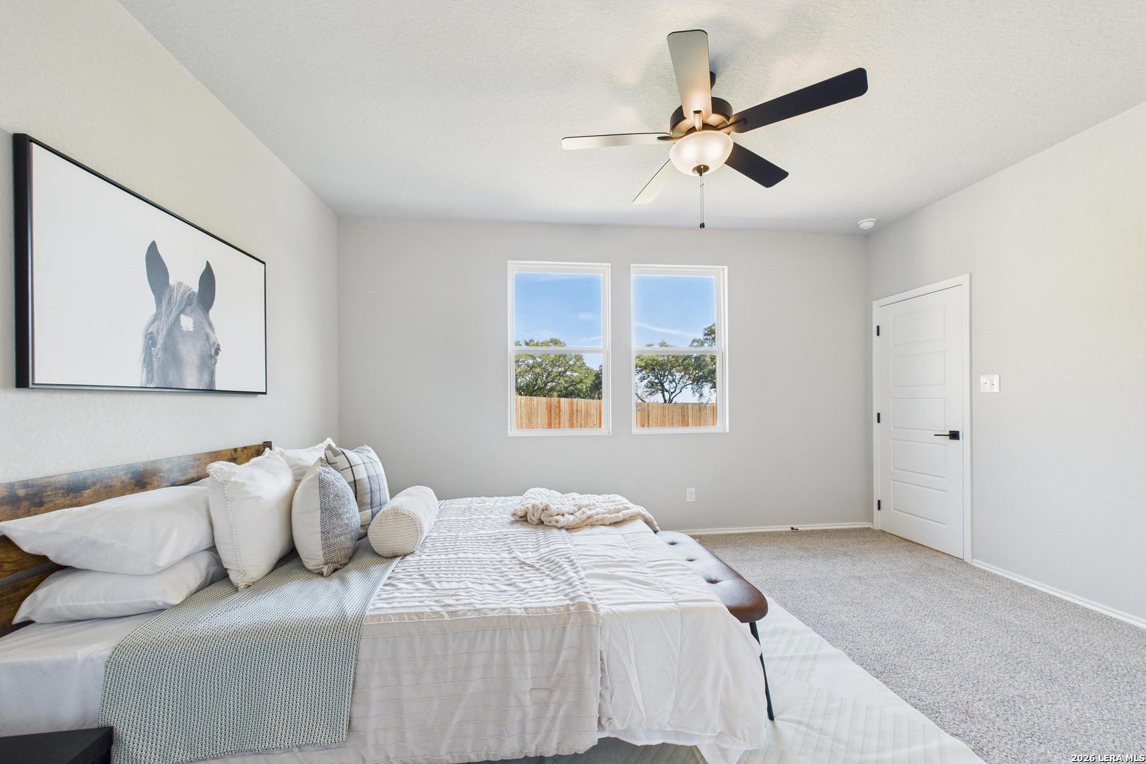 Elegant master bedroom with light gray walls, large windows, ceiling fan, king bed, and equestrian art in Davidson Homes The Douglas E, Bricewood, San Antonio