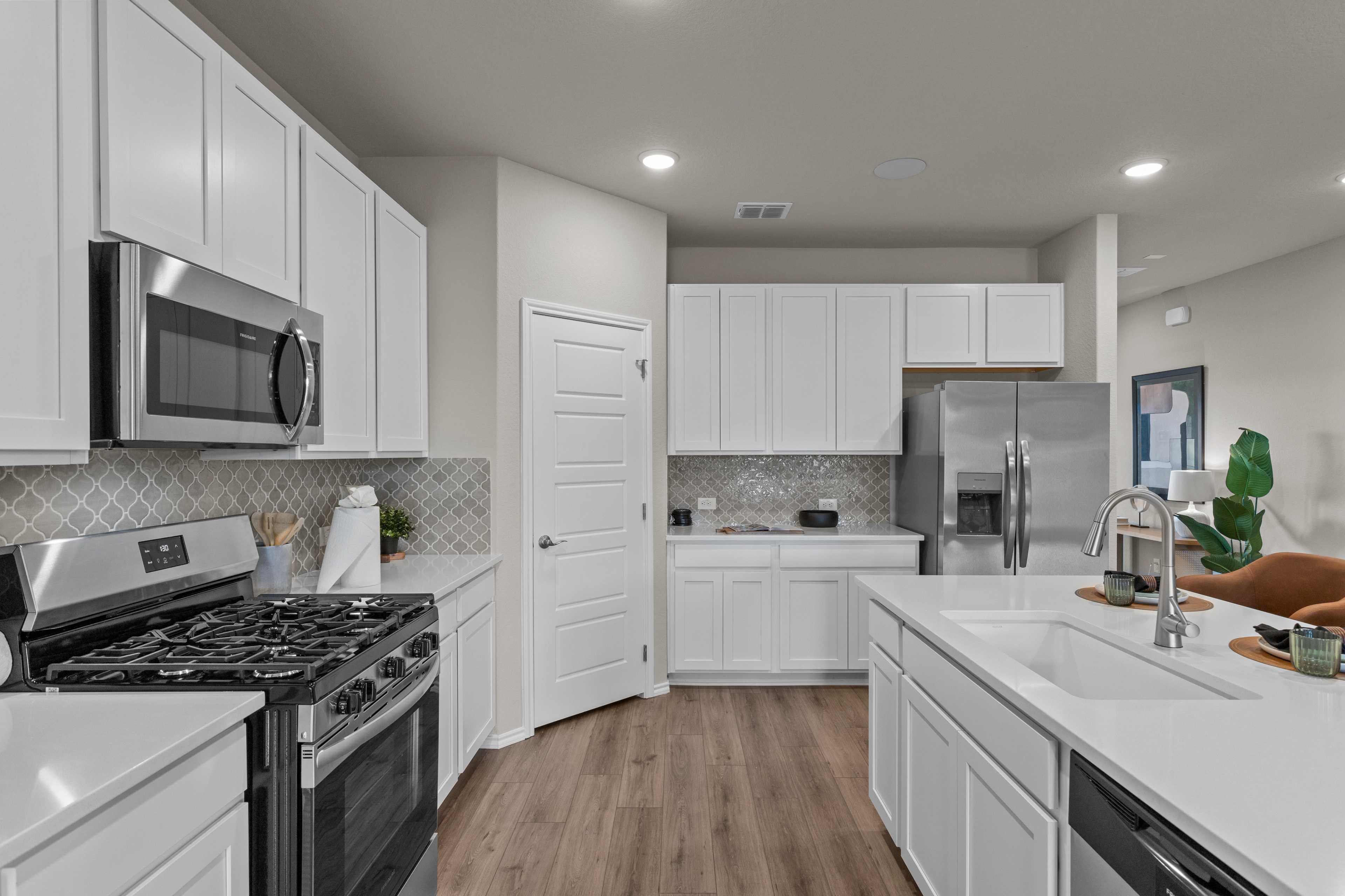 Modern kitchen at Comanche Ridge in San Antonio TX by Davidson Homes featuring white cabinets, stainless steel appliances, and hardwood floors