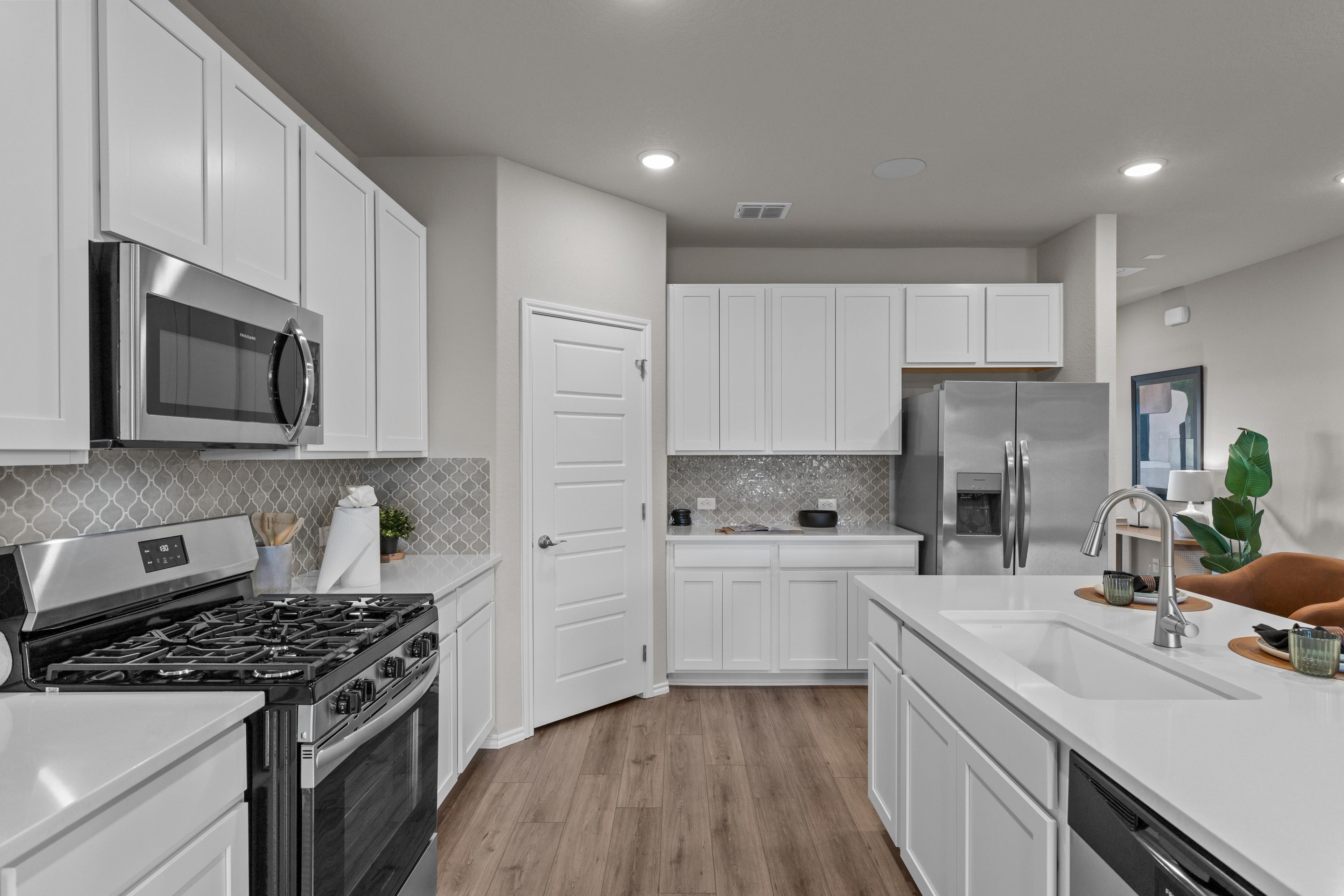 Modern kitchen at Comanche Ridge in San Antonio TX by Davidson Homes featuring white cabinets, stainless steel appliances, and hardwood floors