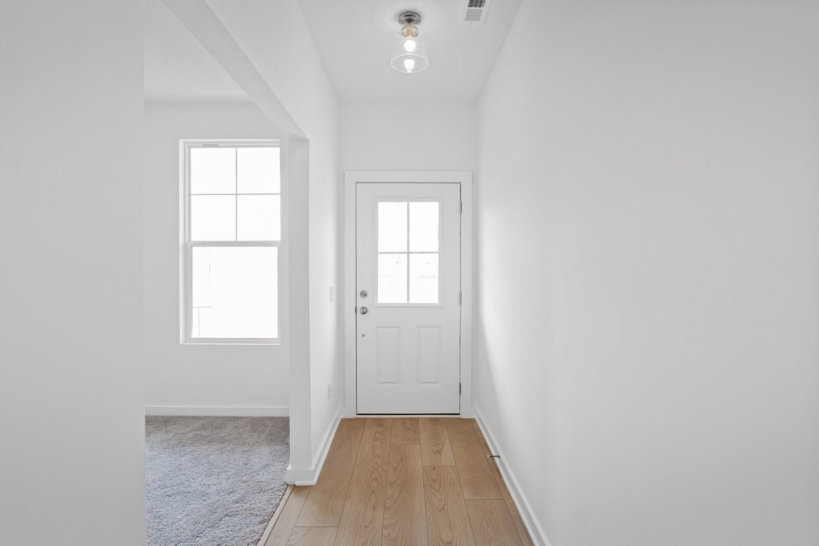 Bright entry hallway with oak hardwood floors, white walls, and glass door in The Logan C by Davidson Homes, White House, TN