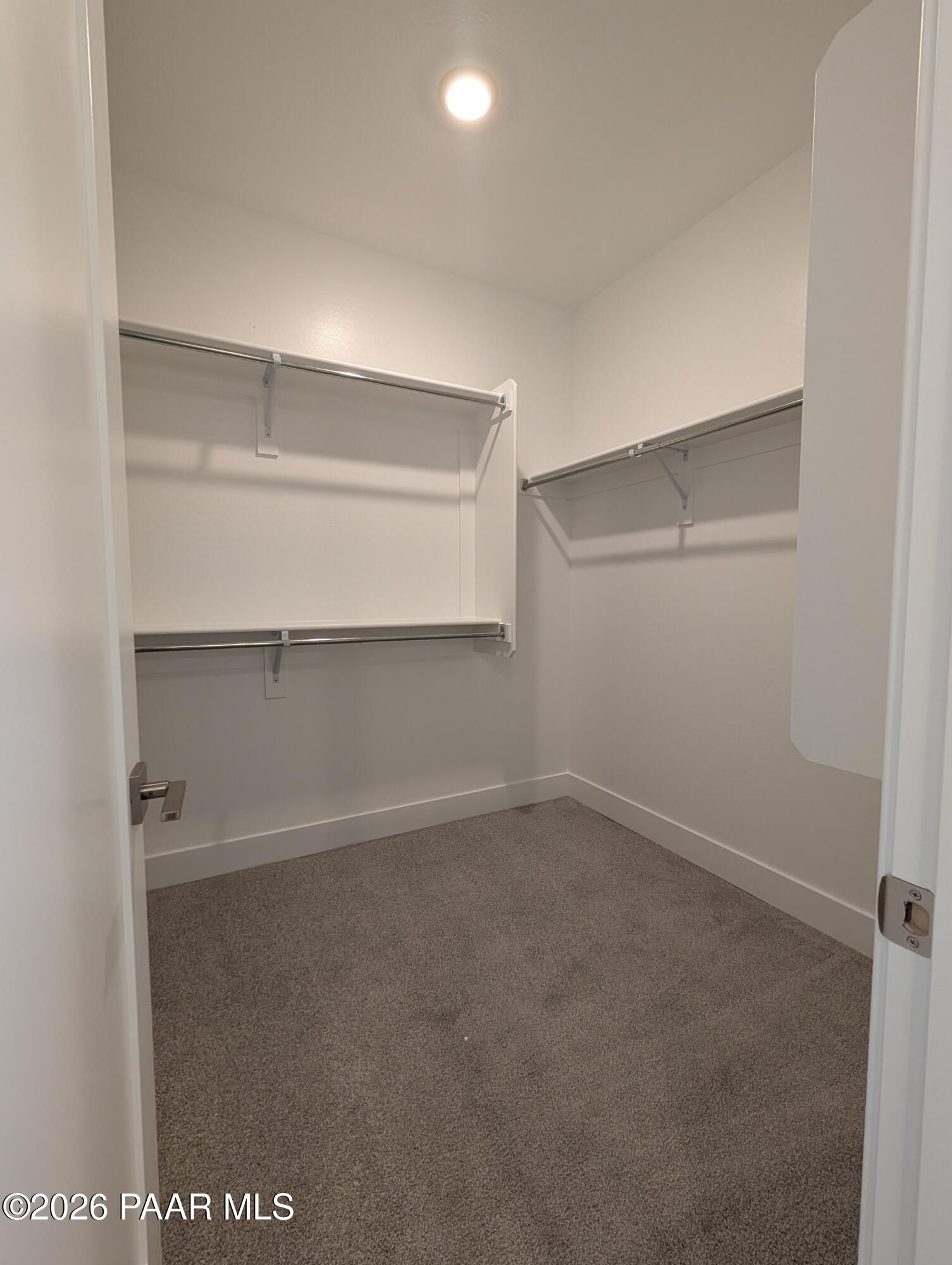Spacious walk-in closet featuring white walls, metal hanging rods, shelves, and gray carpet in Davidson Homes The Durango II F, Prescott, Arizona