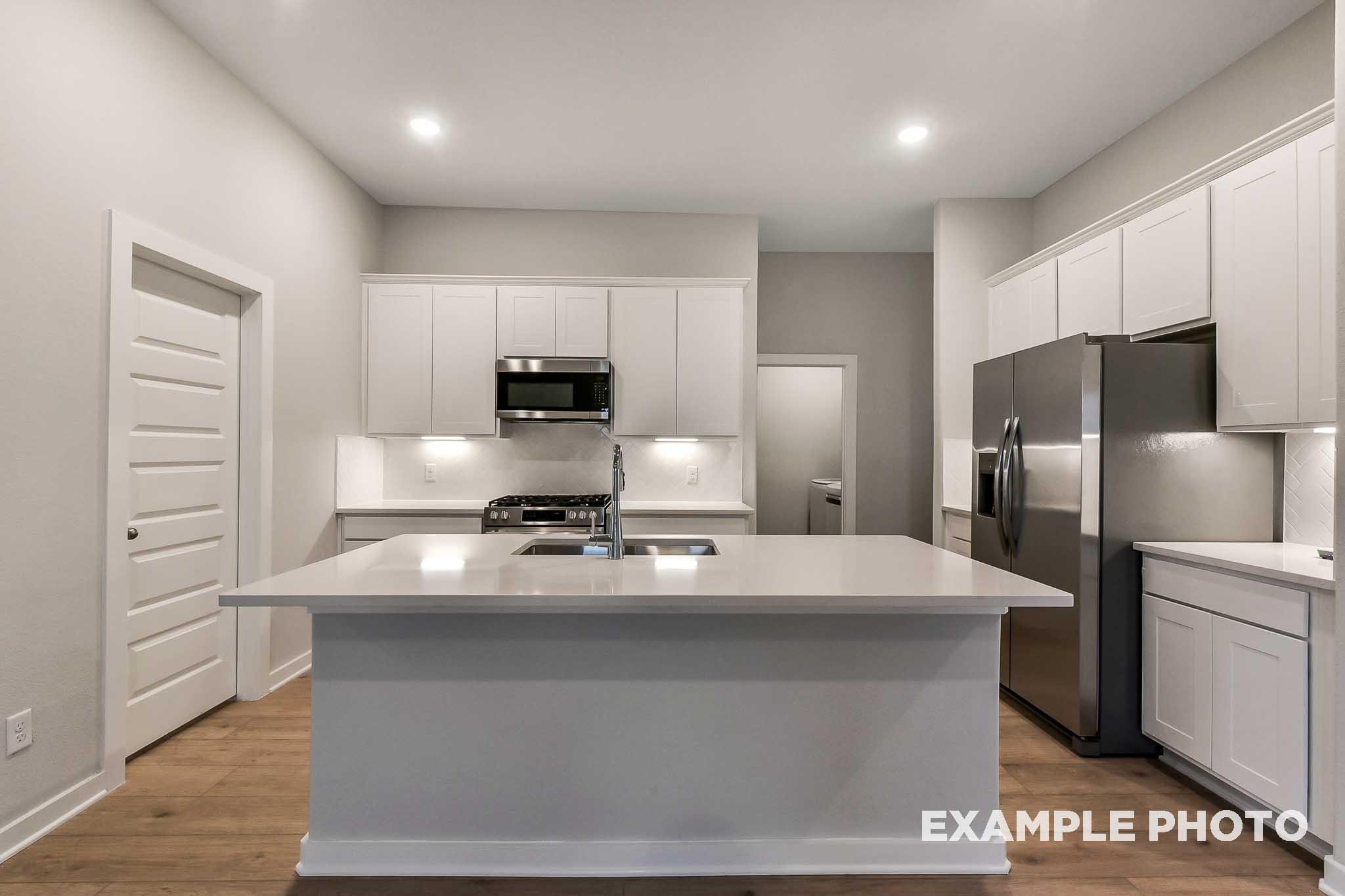 Spacious modern kitchen in The Laguna B with white shaker cabinets, quartz island sink, stainless steel appliances
