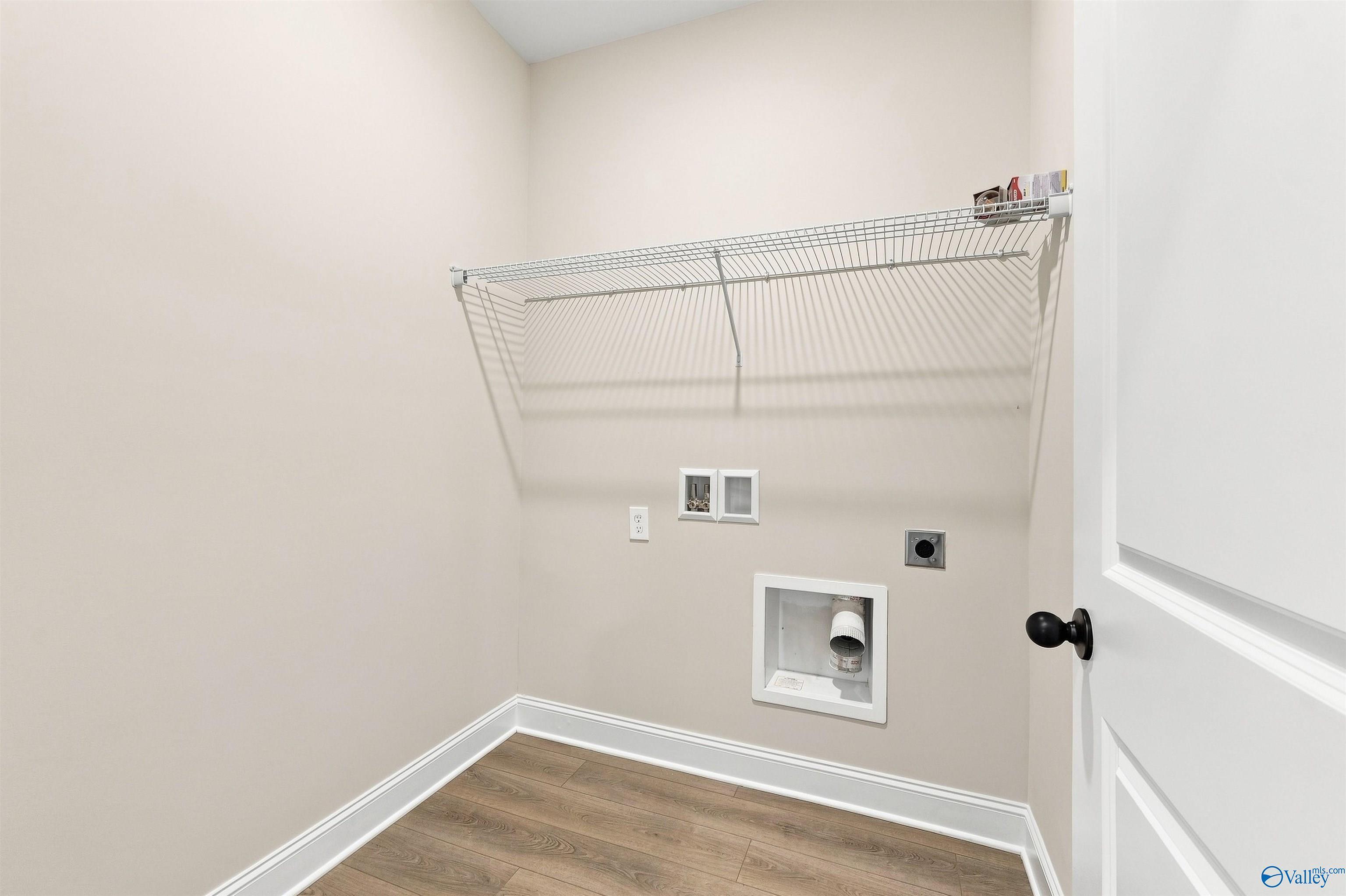 Wire shelf above washer-dryer hookups with vinyl plank flooring in laundry room of Davidson Homes Franklin C, Athens, AL