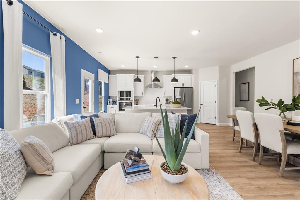Spacious open-concept living room with blue accent wall, L-shaped sofa, dining table, and modern kitchen in Davidson Homes The Burton C, Canton, Georgia