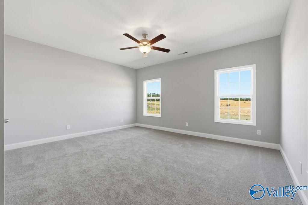 Bright bedroom with gray walls, carpeted floor, ceiling fan, and large windows overlooking fields in Davidson Homes The Harrison, Hartselle, AL