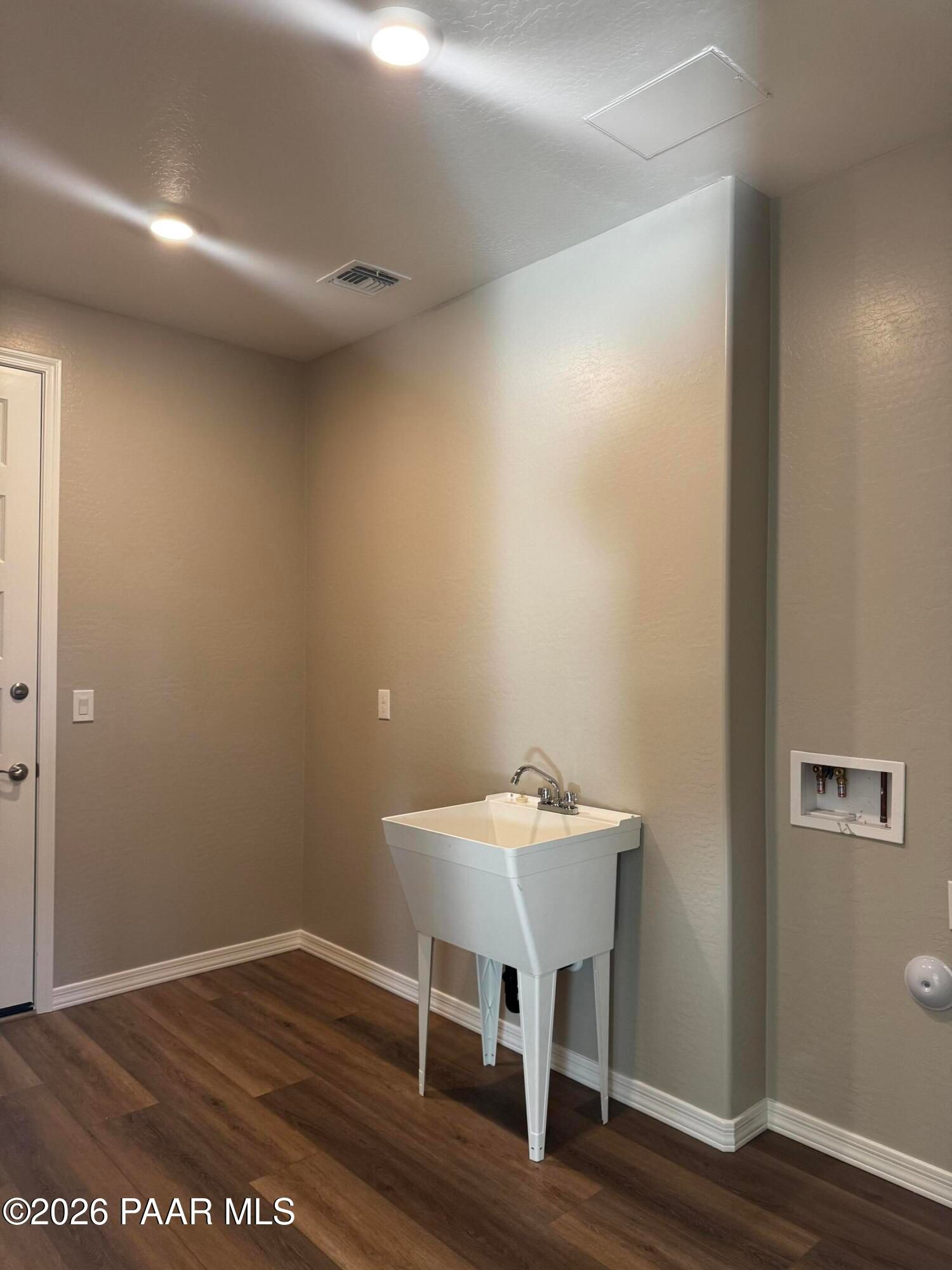 Utility laundry room with white pedestal sink, beige walls, and laminate flooring in Davidson Homes The Daybreak B, Prescott Arizona