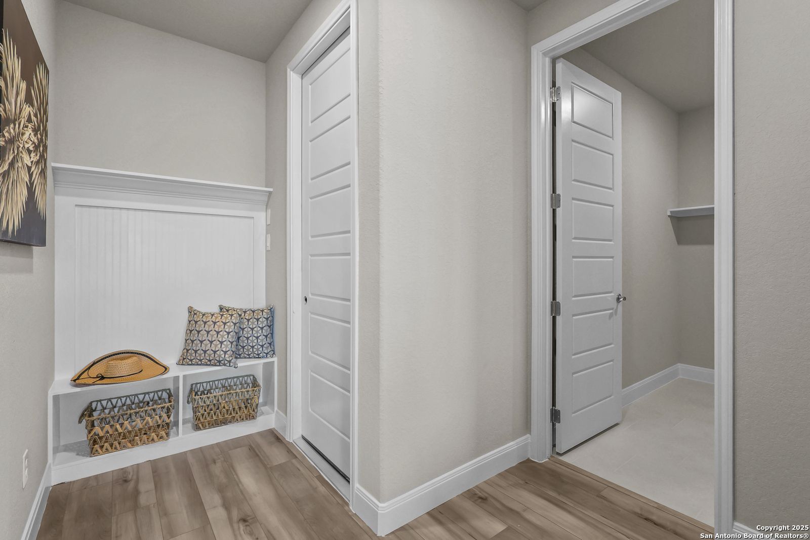 Cozy built-in hallway bench with pillows and wicker baskets, white doors, neutral walls in Davidson Homes The Jennings G, Castroville Texas