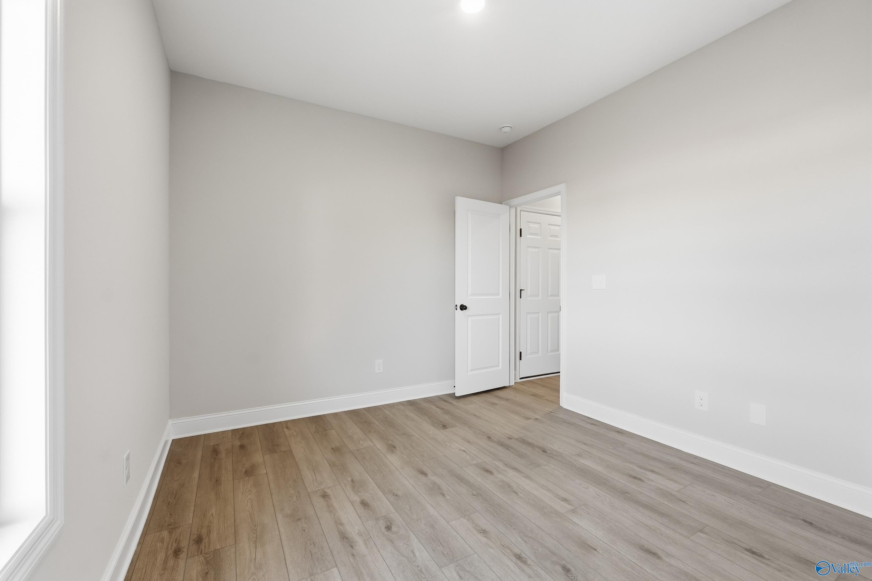 Bright secondary bedroom with light gray walls, hardwood floors, and natural light in Davidson Homes The Daphne C, Athens, Alabama