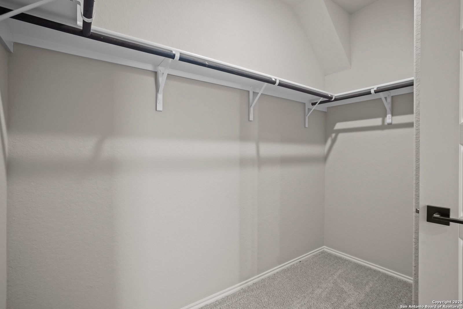 Spacious walk-in closet with black hanging rods, gray carpet, and neutral walls in The Asheville H by Davidson Homes, Converse, Texas