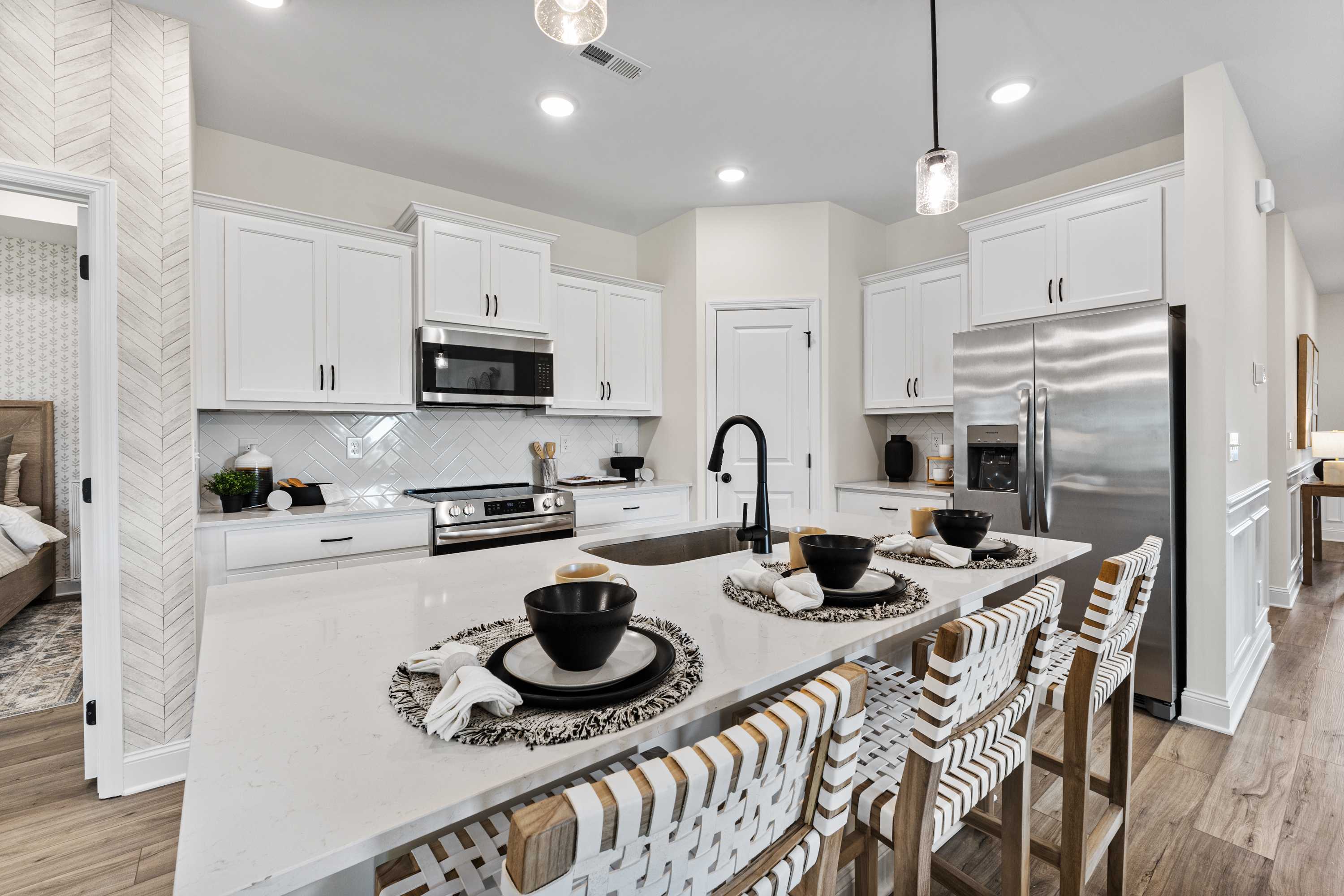 Modern open-concept kitchen in Lynn Meadows Meridianville AL with white shaker cabinets, stainless steel appliances, and woven bar stools at island