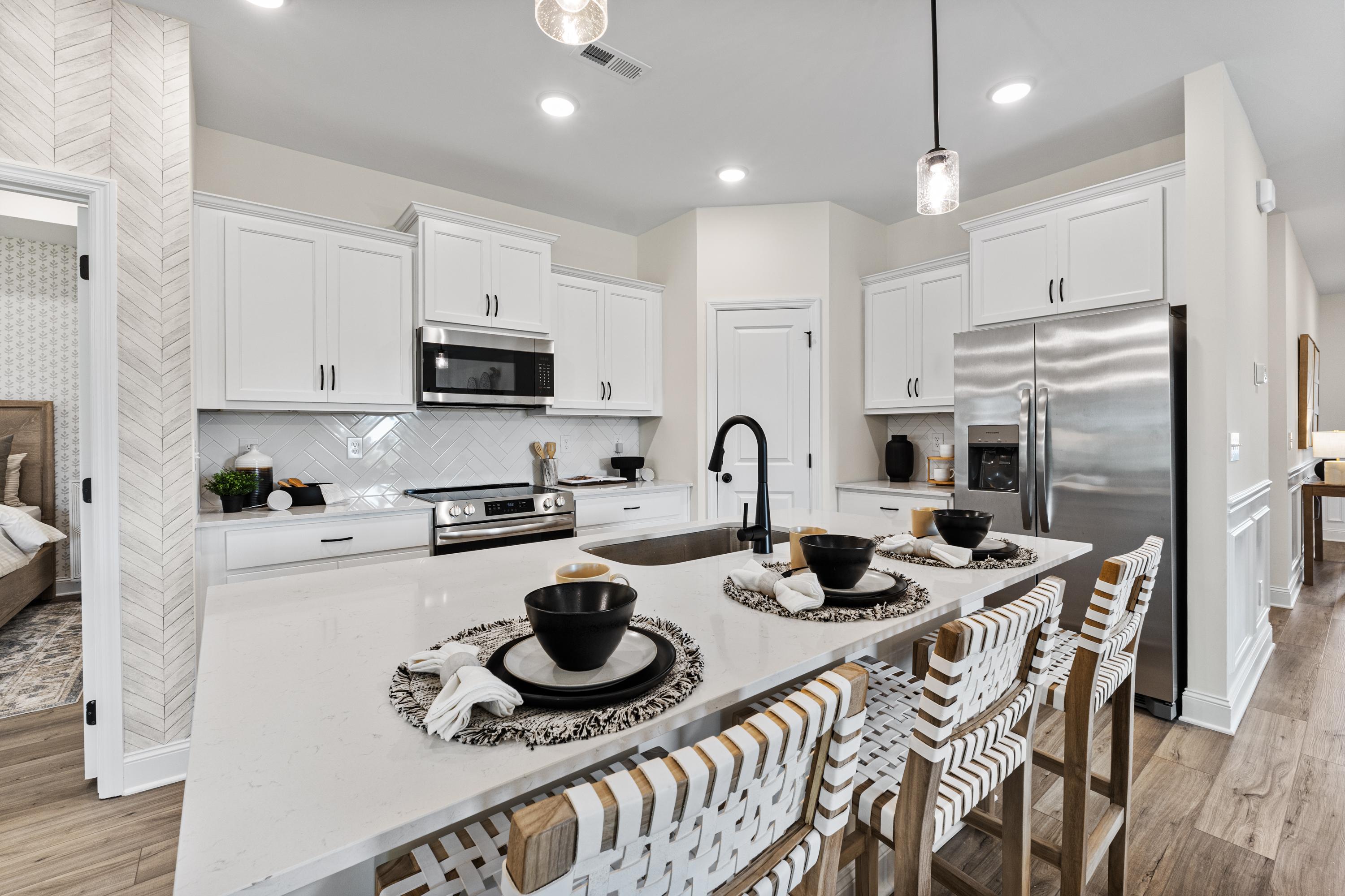 Modern open-concept kitchen in Lynn Meadows Meridianville AL with white shaker cabinets, stainless steel appliances, and woven bar stools at island