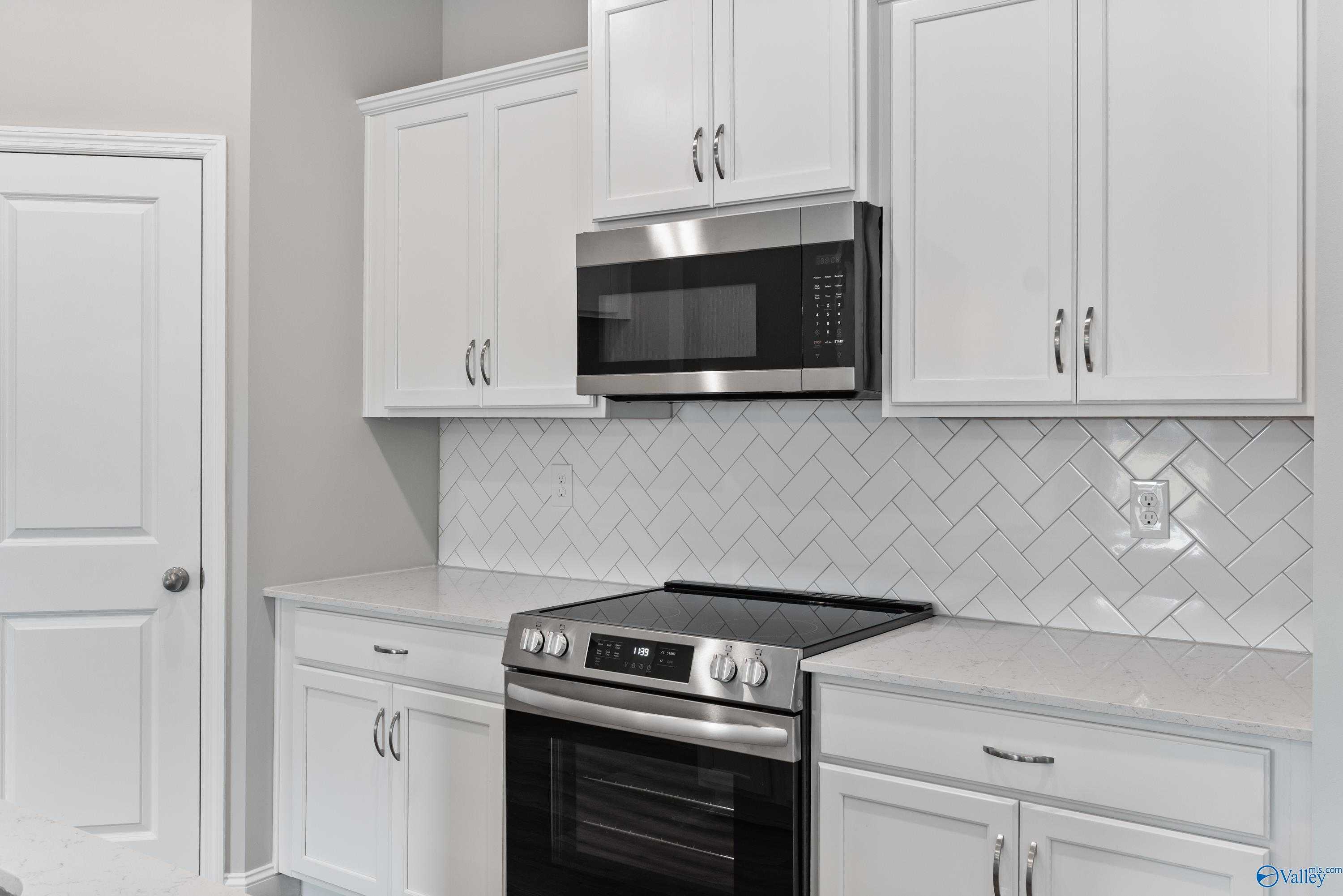 Modern white shaker kitchen with stainless appliances, herringbone subway tile backsplash in Davidson Homes The Franklin, Huntsville AL