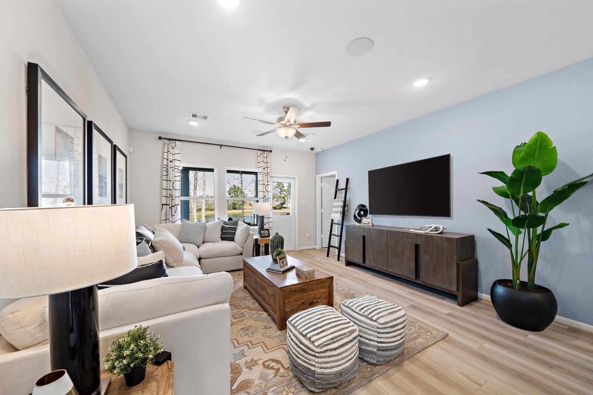 Modern living room at Saddle Creek Ranch in Cibolo Texas by Davidson Homes with white L-shaped sofa, hardwood floors, and large windows