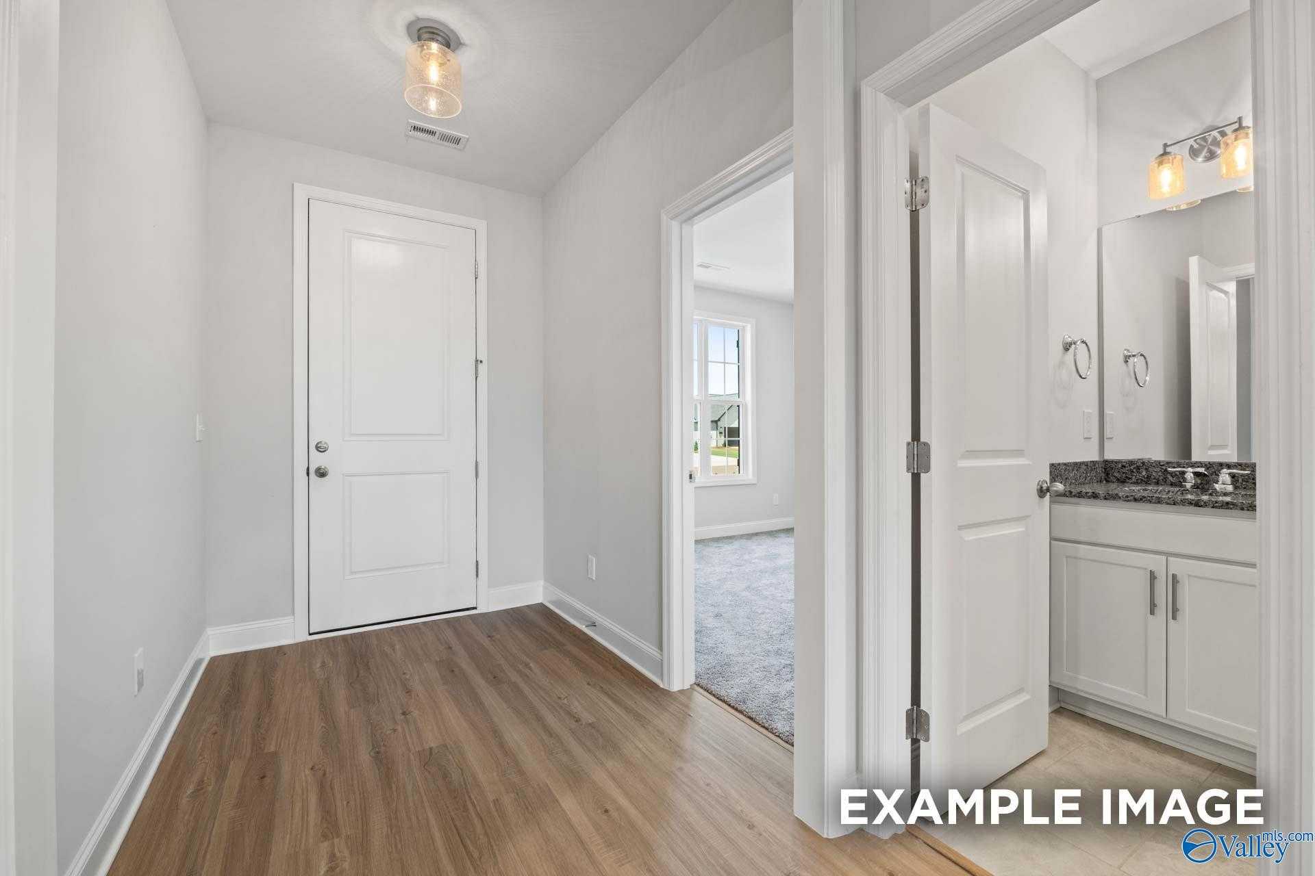 Modern bathroom with granite vanity, white cabinets, and mirror off wood-floored hallway in The Lanier plan, Davidson Homes, Meridianville