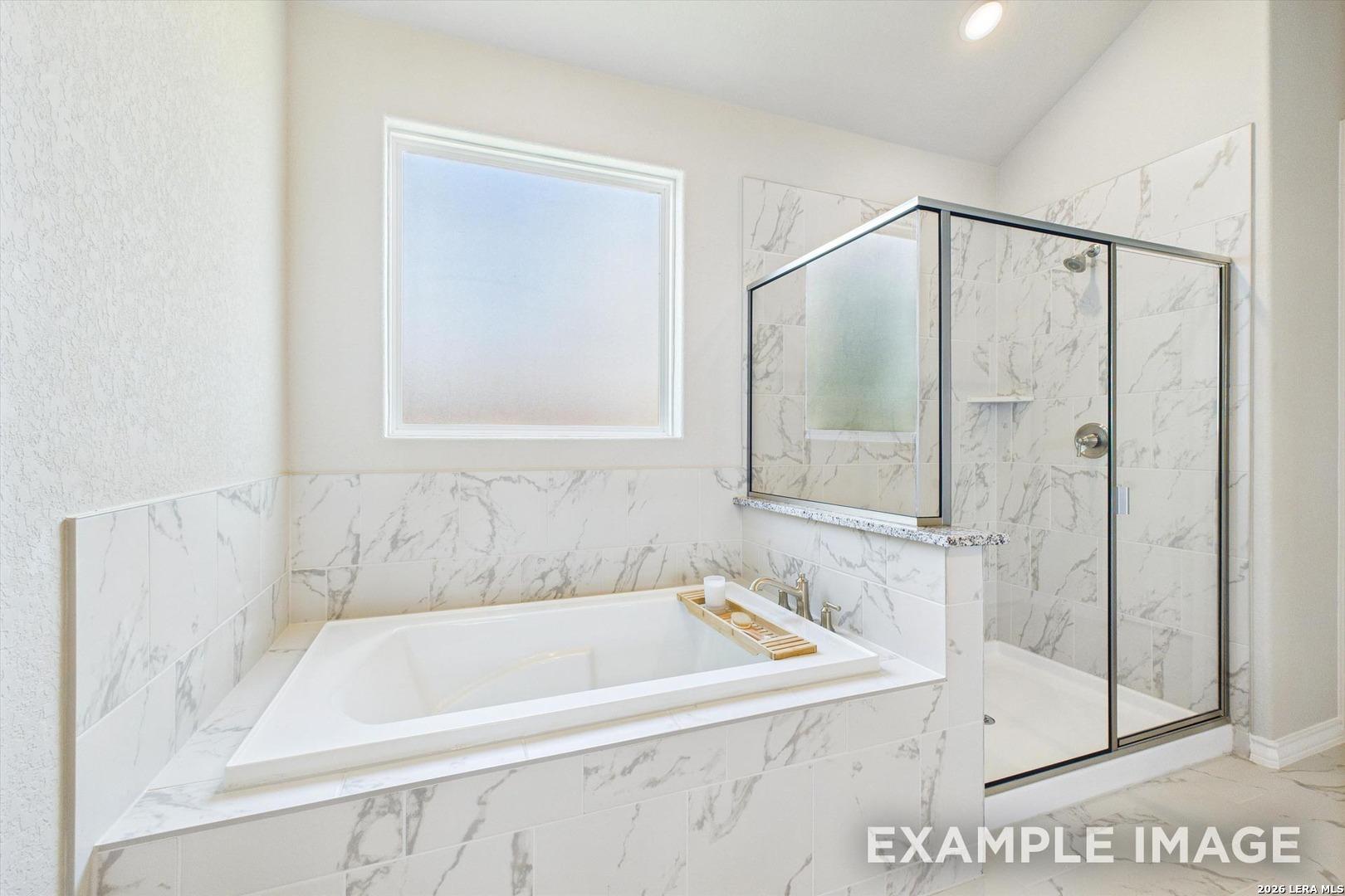 Luxurious primary bathroom with marble-tiled soaking tub and glass shower in The Foster F home at Potranco Oaks, TX.